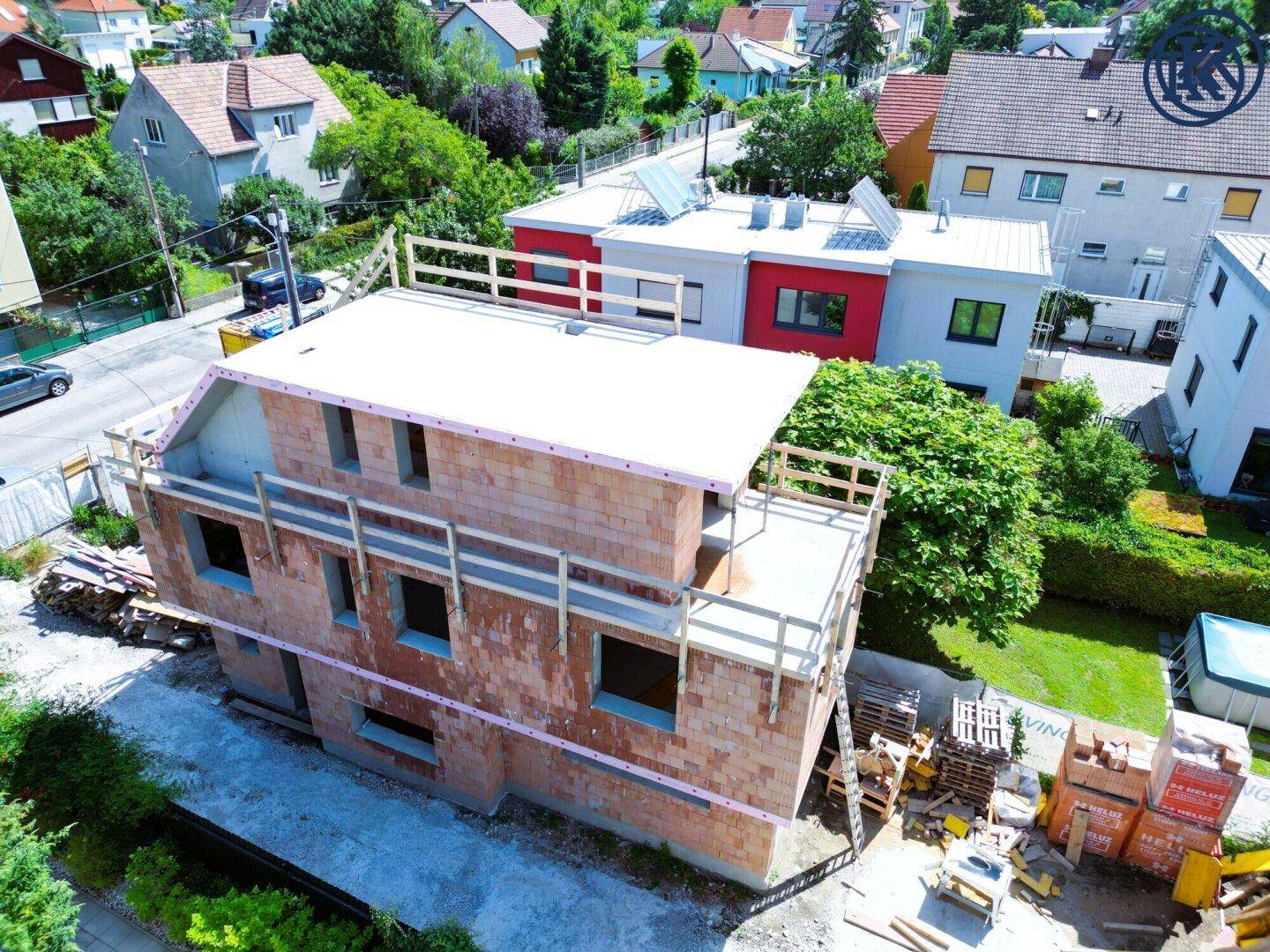 Haus im Rohbau mit sichtbaren Ziegelwänden und Gerüst, umgeben von weiteren Wohnhäusern.