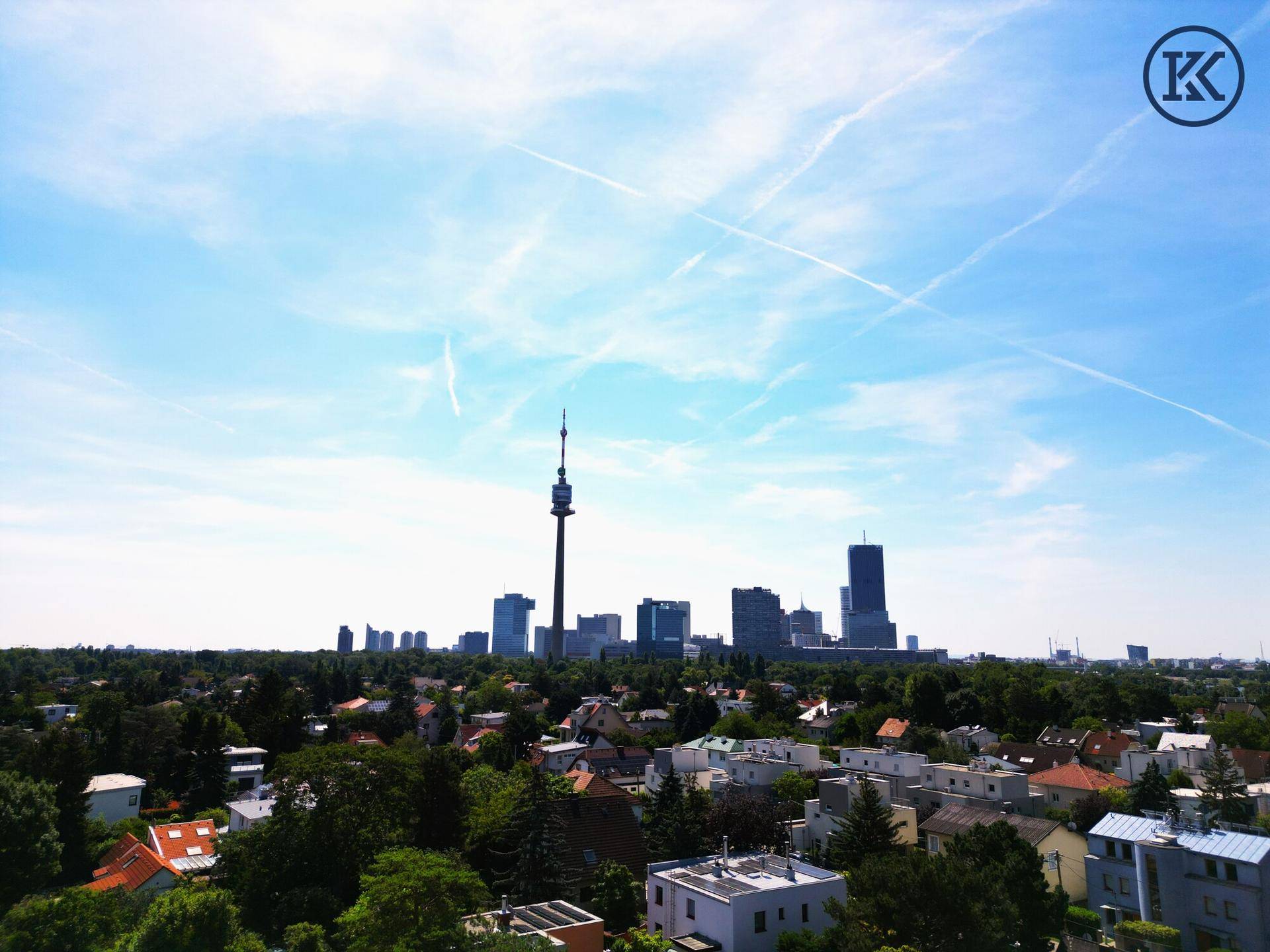 Panoramablick auf die Wiener Skyline mit dem Donauturm und umliegenden Wohngebieten unter blauem Himmel.