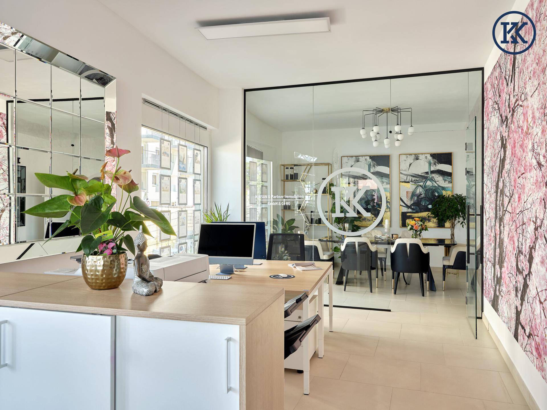 Modernes Büro mit Schreibtisch, Glaswand zum Besprechungsraum und auffälliger Kirschblüten-Tapete.