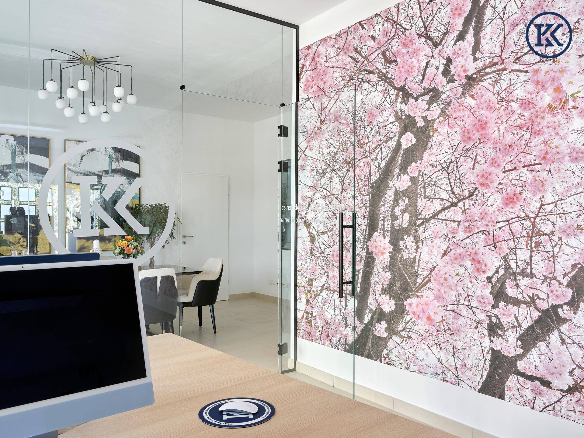 Blick vom Büroschreibtisch in den Besprechungsraum, getrennt durch eine Glaswand mit Kirschblüten-Tapete.