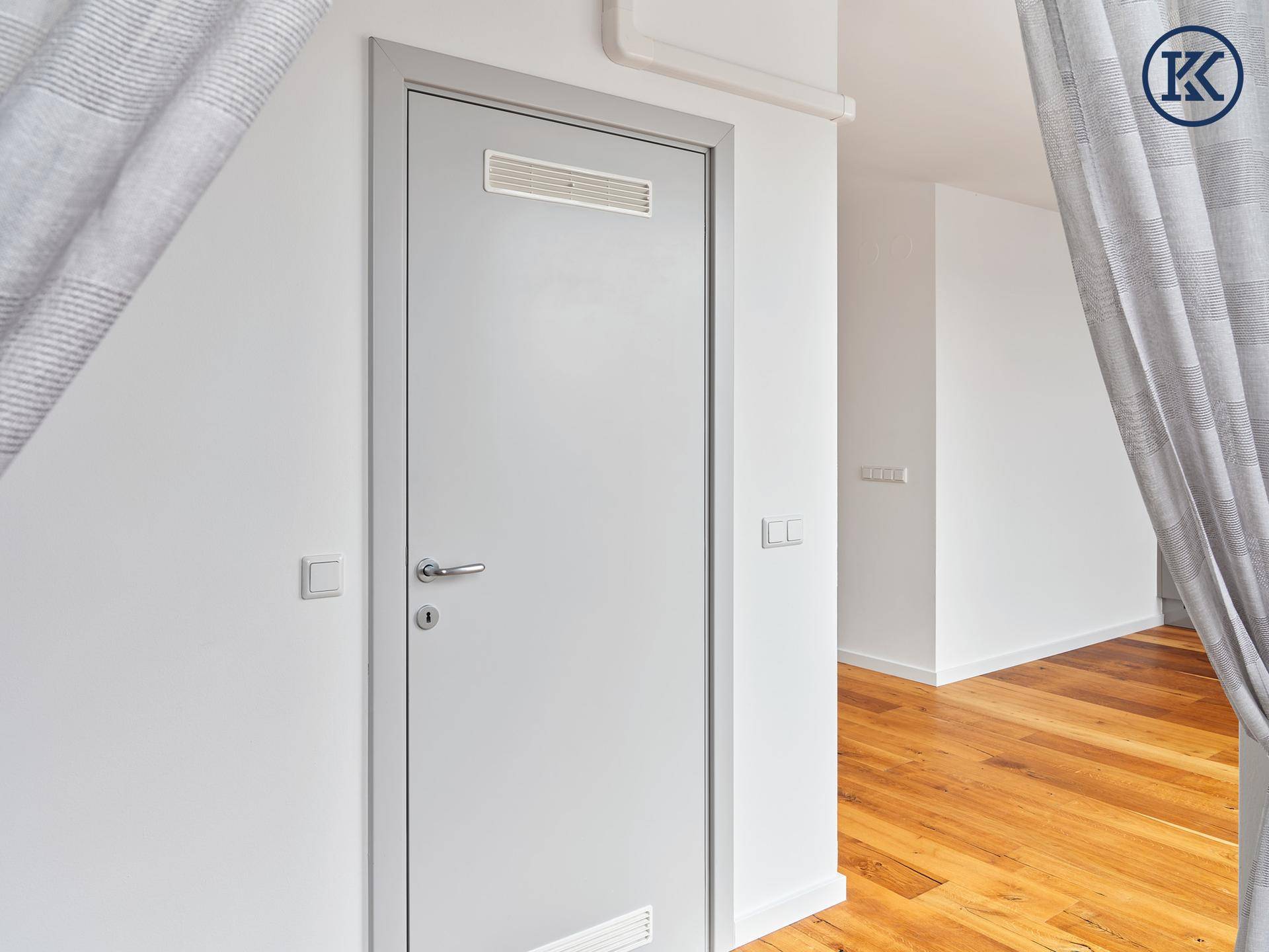 Heller Flur mit Holzboden und einer modernen Tür, die in einen weiteren Raum führt.