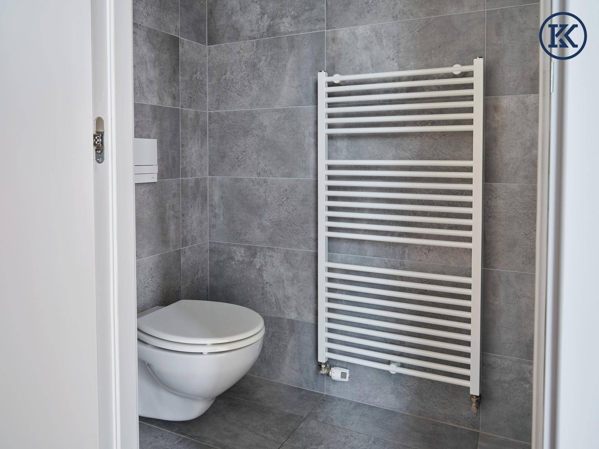 Modernes WC mit grauen Fliesen, wandhängender Toilette und beheiztem Handtuchhalter.
