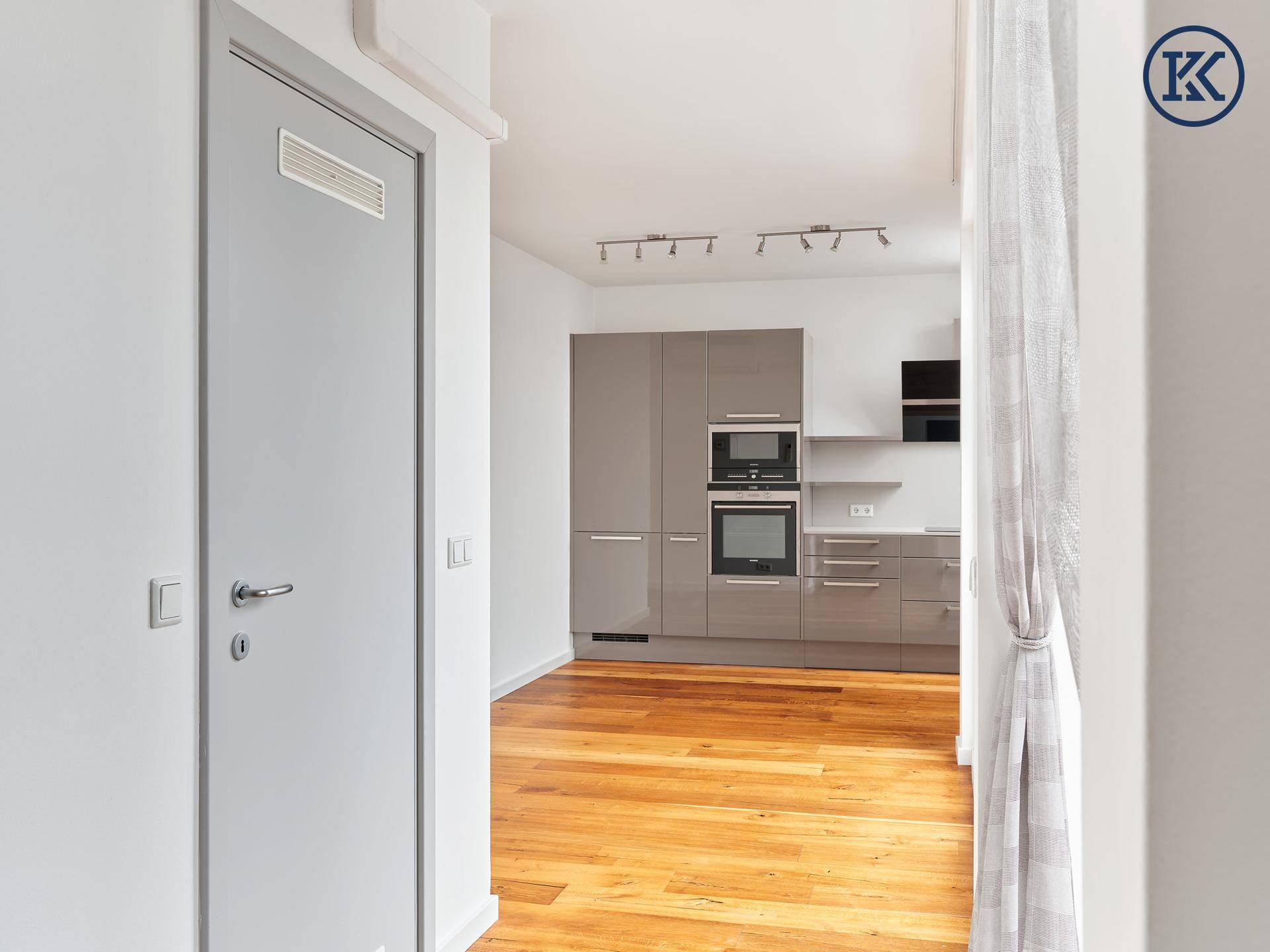 Blick vom Flur in die moderne Küche mit grauen Schränken und Holzboden.