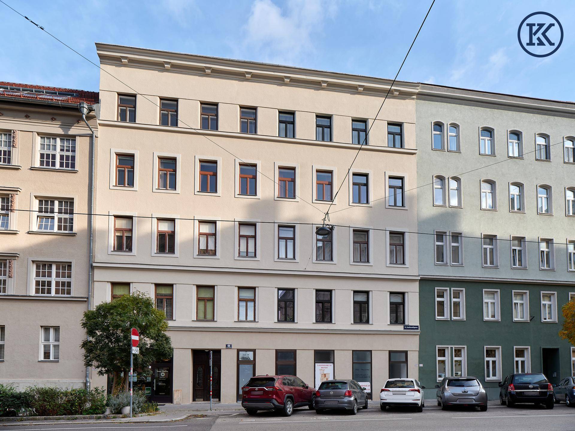 Ansicht eines gepflegten Mehrfamilienhauses mit mehreren Etagen und parkenden Fahrzeugen davor.