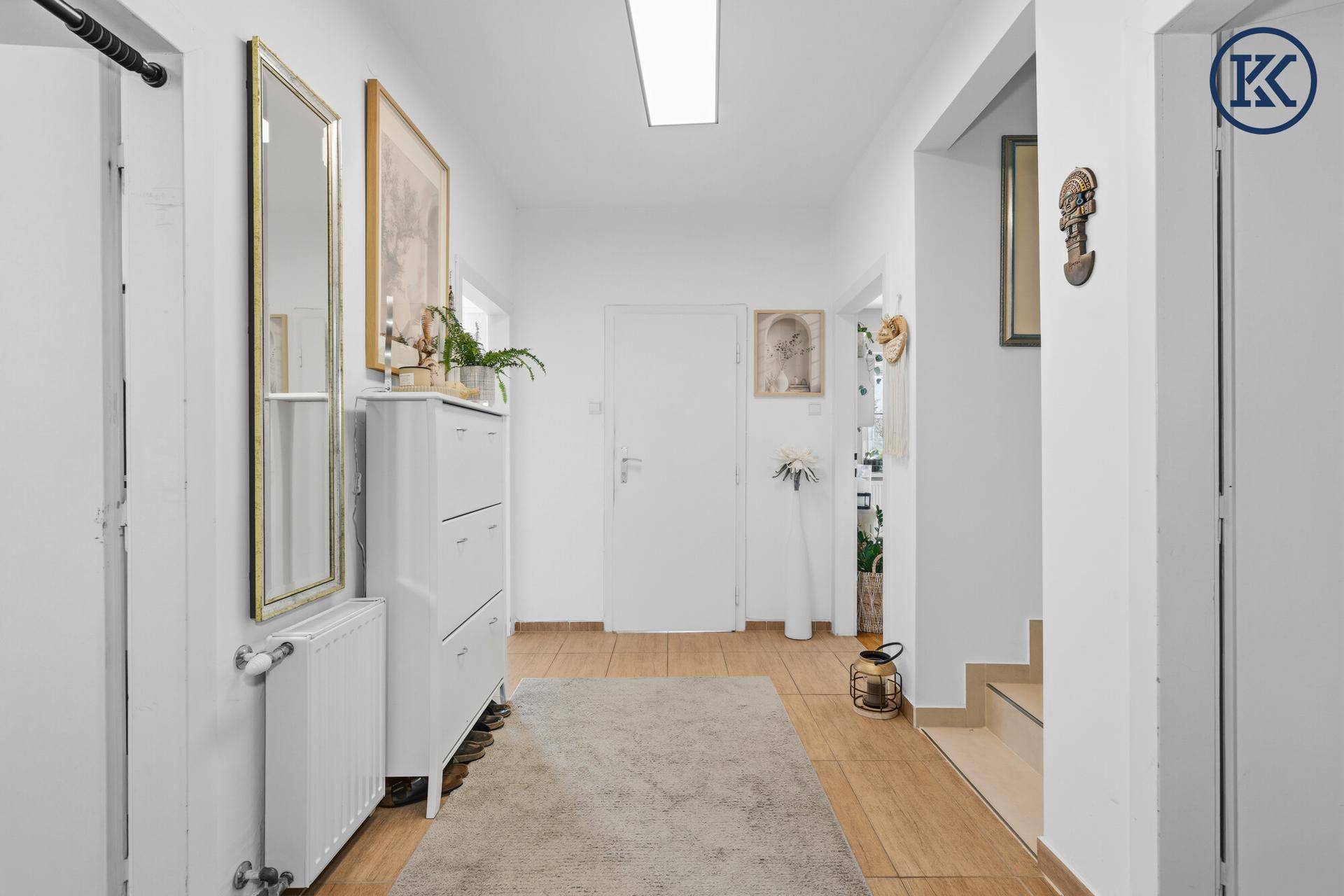 Langer, heller Flur mit Holzfußboden, weißer Kommode und Spiegel, der viel Licht reflektiert.