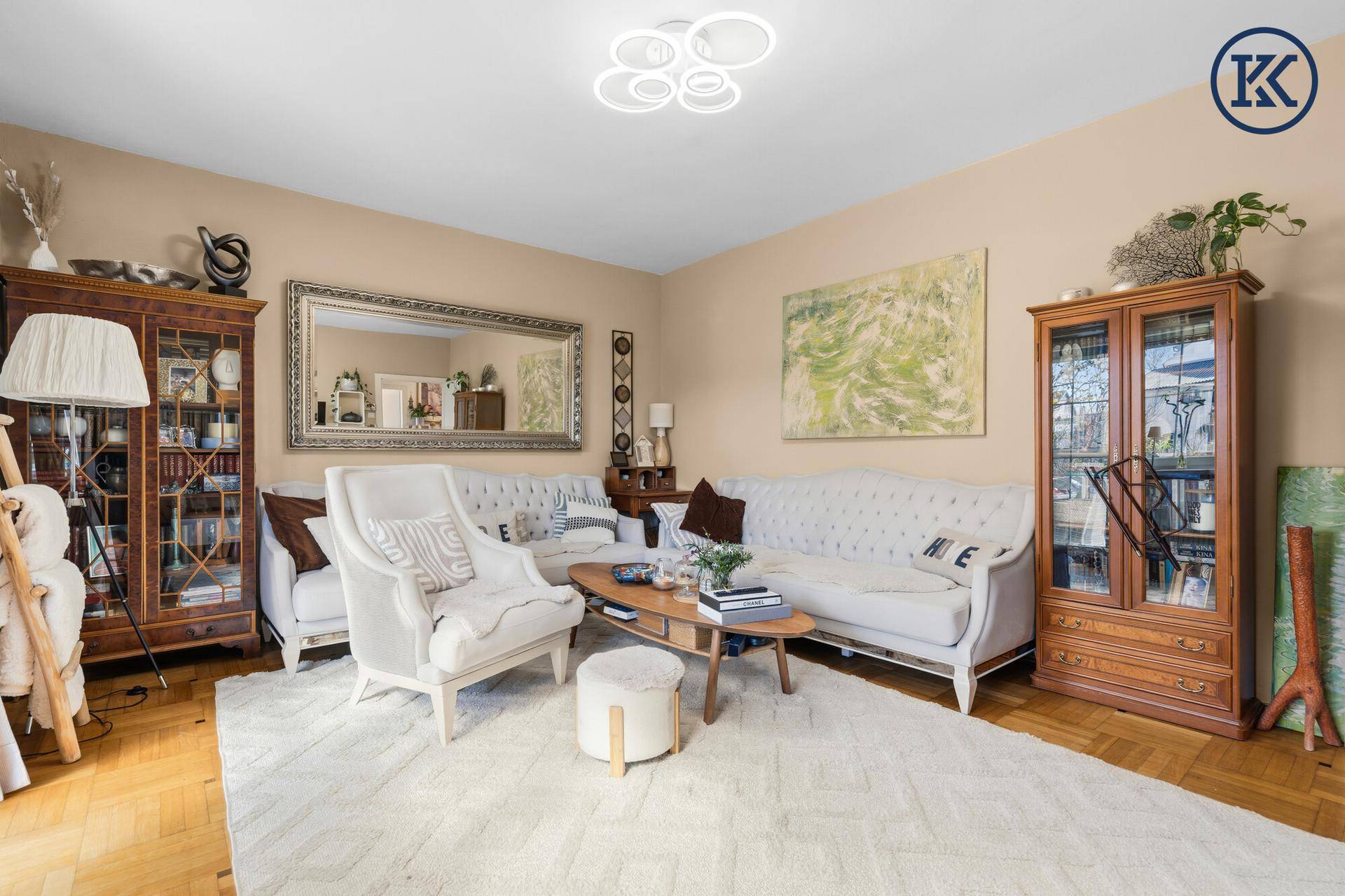 Elegantes Wohnzimmer mit beigen Wänden, Parkettboden und stilvollen Vitrinen.
