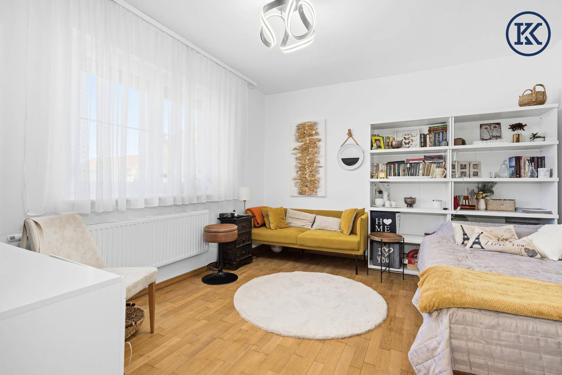 Helles Schlafzimmer mit Holzfußboden, gelbem Sofa und großem Bücherregal.