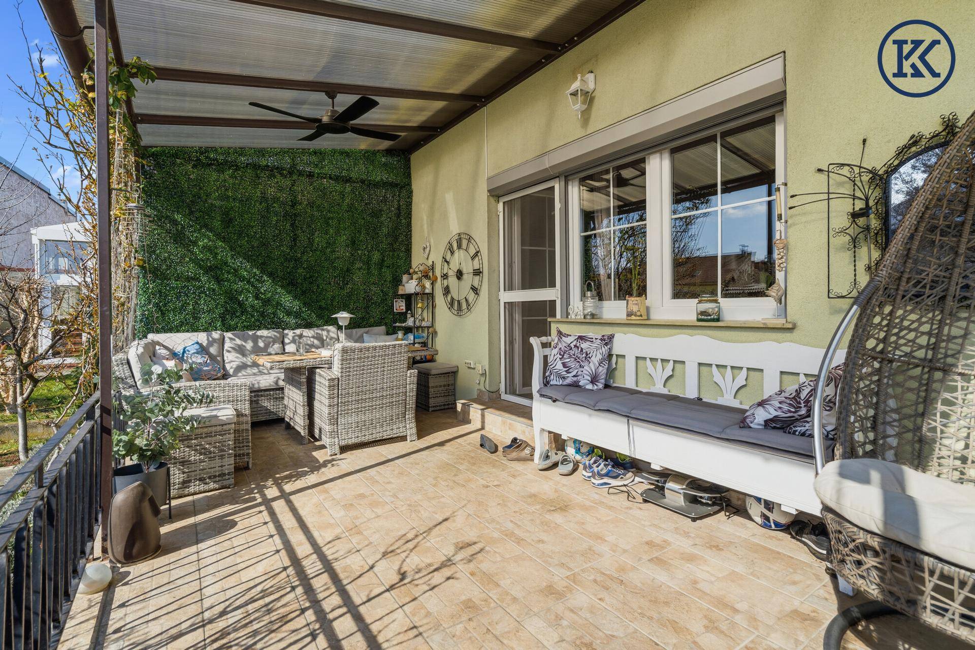 Überdachte Terrasse mit Sitzgelegenheiten, Deckenventilator und Blick in den Garten.