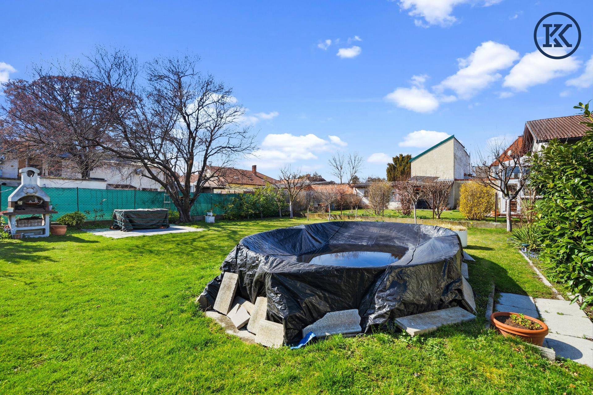 Großer Garten mit Rasenfläche, Pool und Grillplatz unter blauem Himmel.