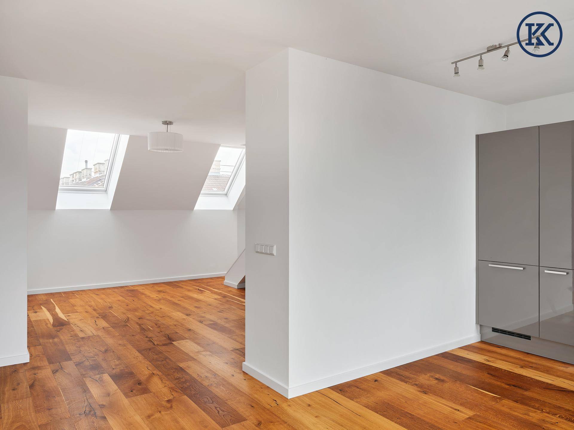 Heller offener Raum mit Holzboden und einem Teil der modernen Küche, beleuchtet durch Dachfenster.