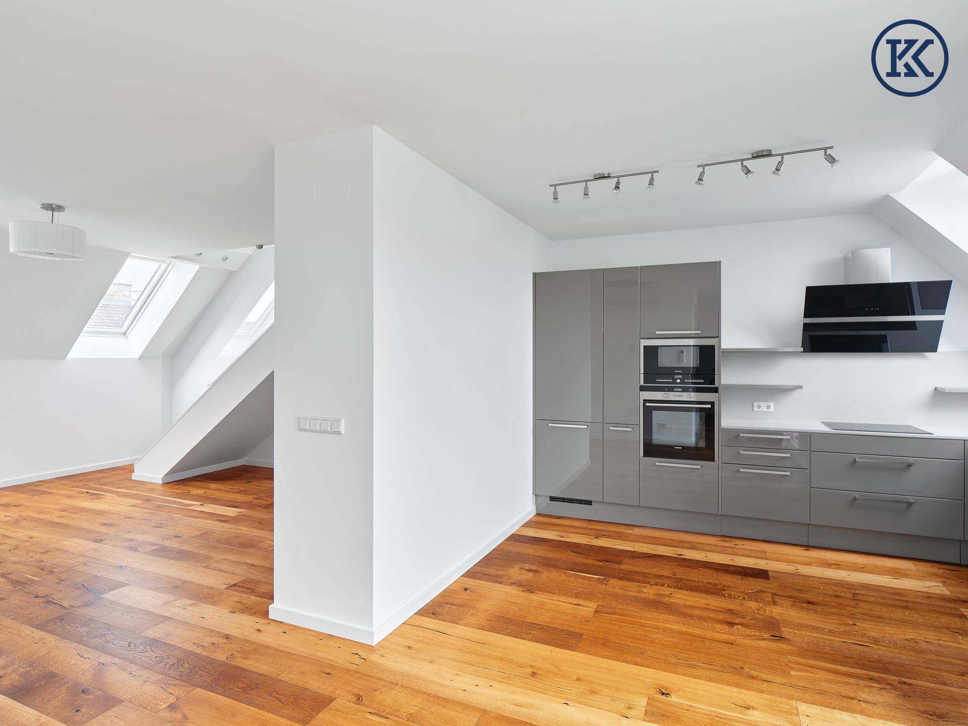 Moderne offene Küche mit grauen Hochglanzfronten, Holzboden und Dachfenstern in einem hellen Raum.