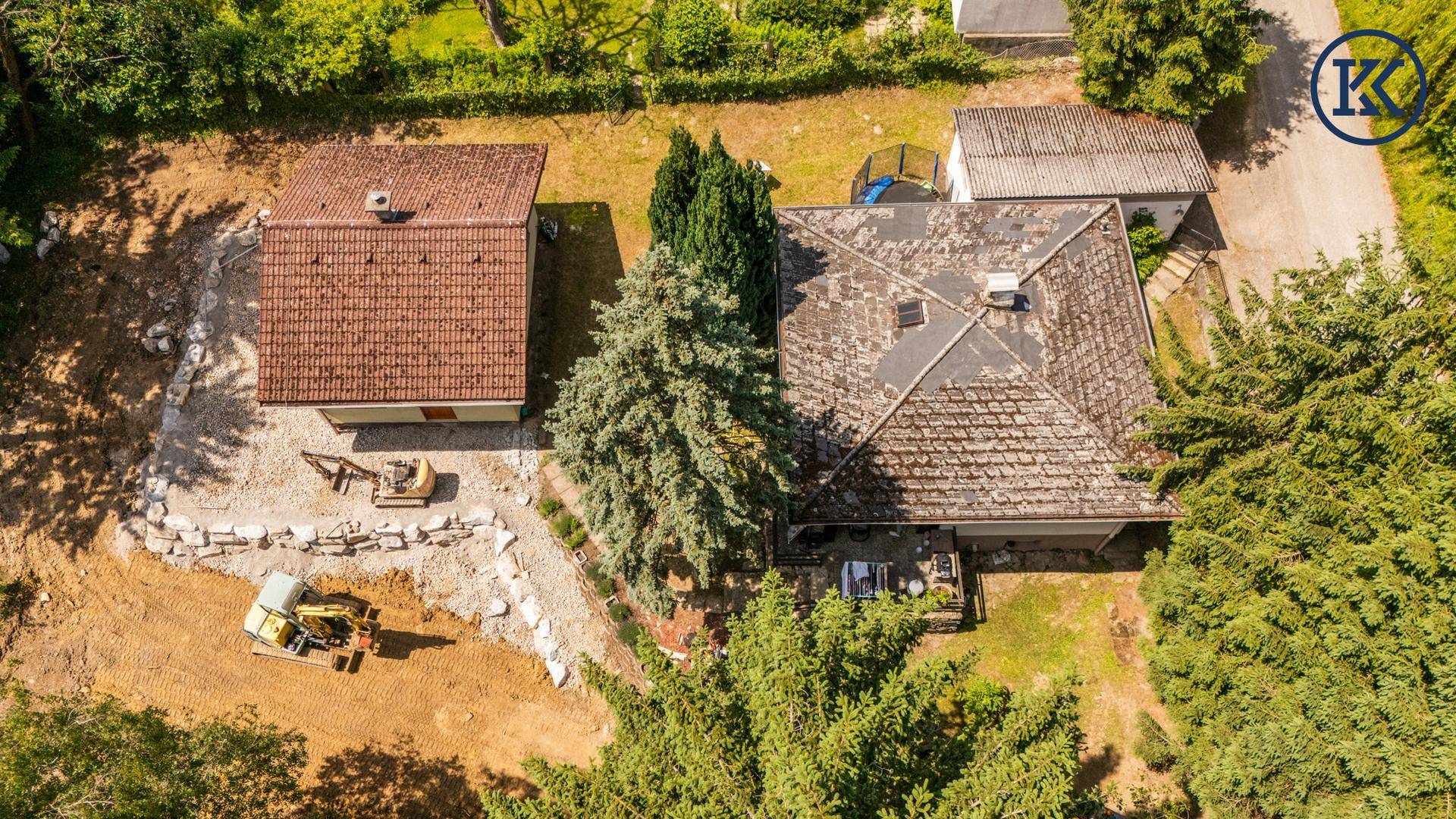 Überblick über das Anwesen mit zwei Gebäuden, viel Grün und einer Baustelle im Vordergrund.