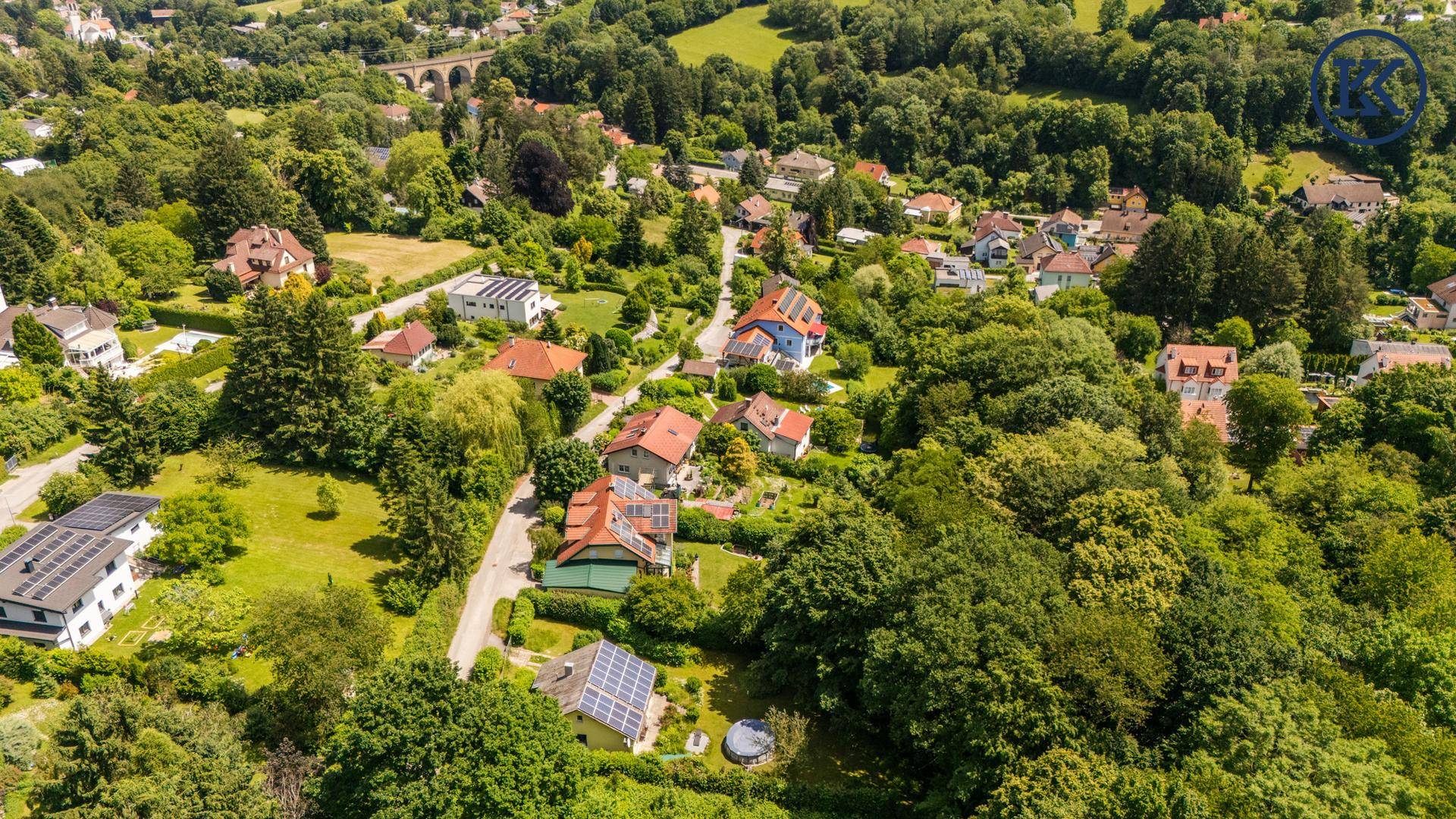 Weitläufige Luftaufnahme der Wohngegend mit vielen Häusern, Bäumen und grünen Hügeln.