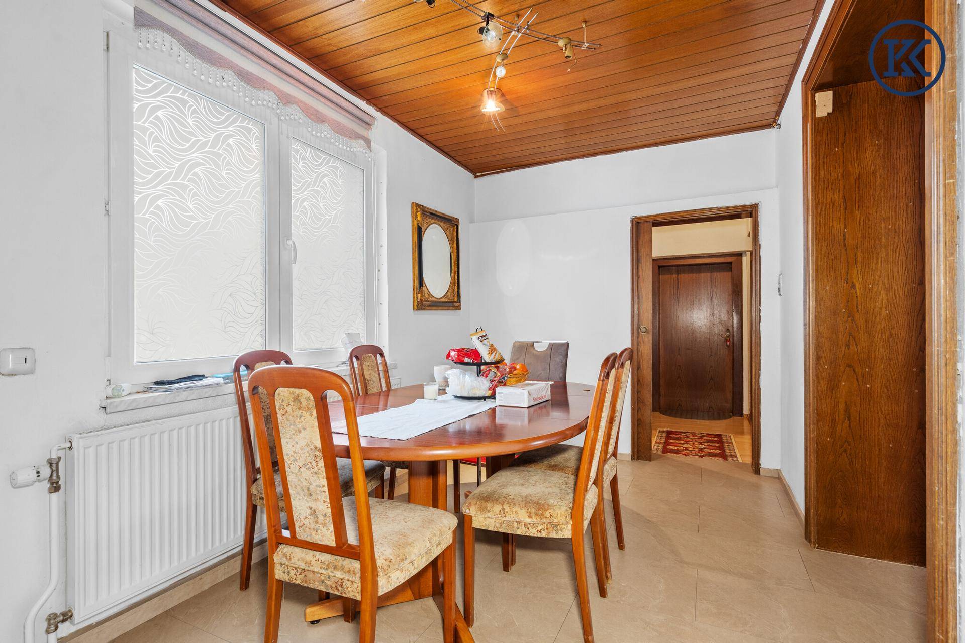 Esszimmer mit Holztisch, Stühlen und einem großen Fenster, das viel Tageslicht hereinlässt.