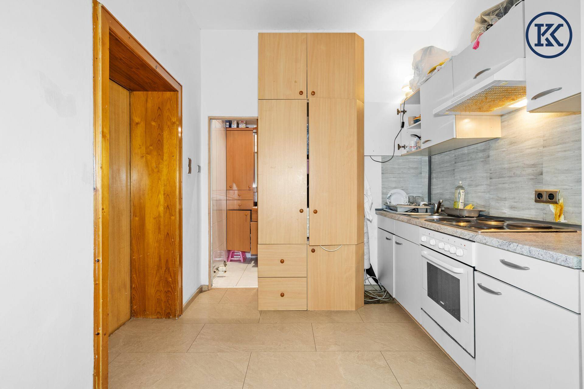 Küche mit weißen Schränken und einem hohen Holzschrank, der zusätzlichen Stauraum bietet.