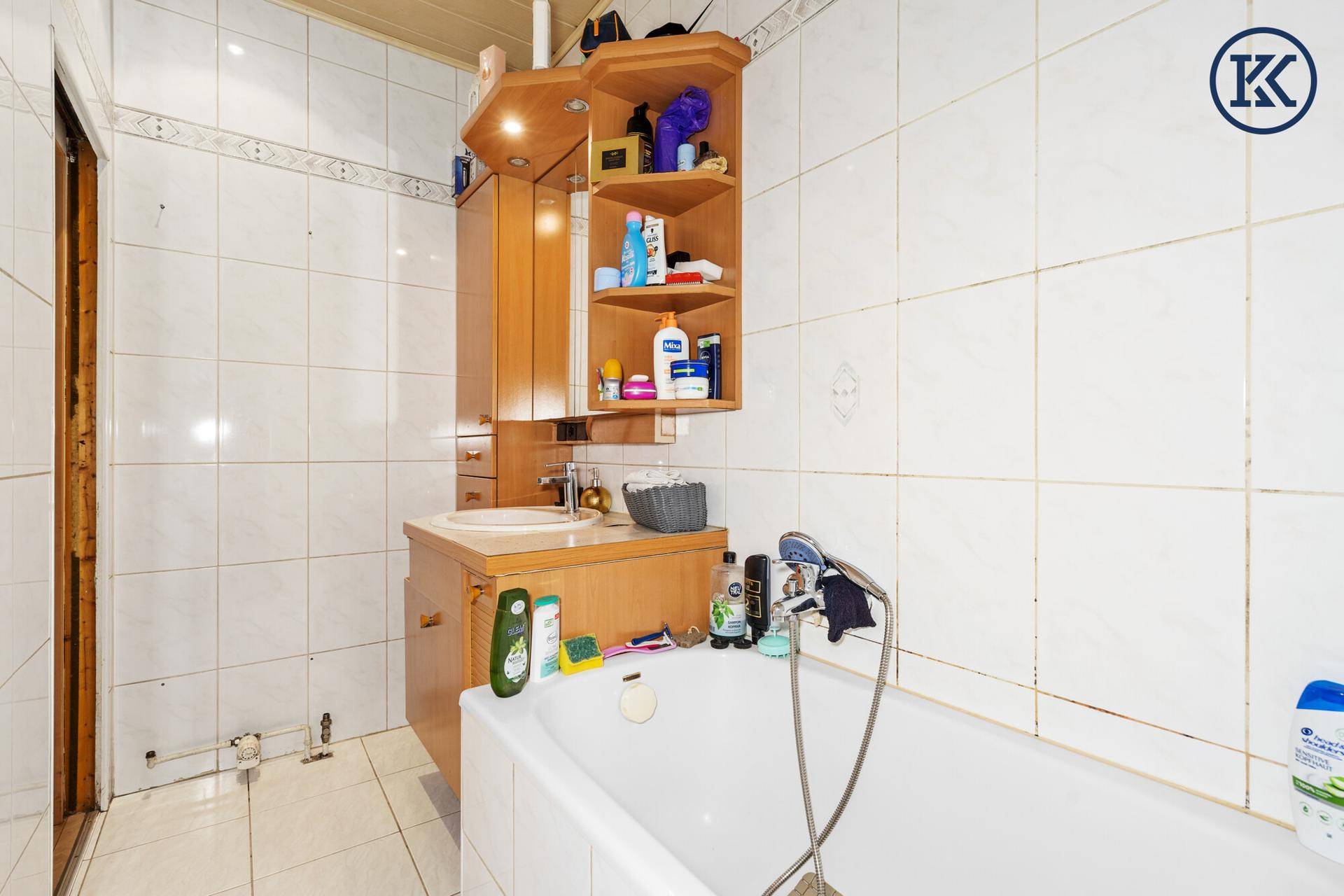 Badezimmer mit Badewanne und Waschbeckenbereich, der zusätzlichen Stauraum bietet.