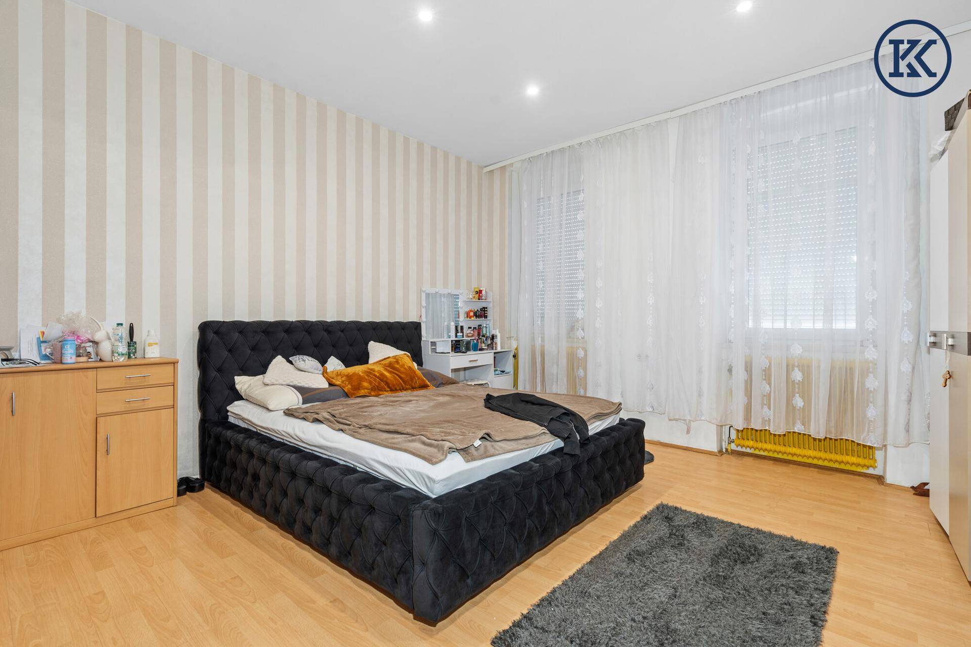 Schlafzimmer mit gestreifter Tapete, großem Doppelbett und hellem Laminatboden.