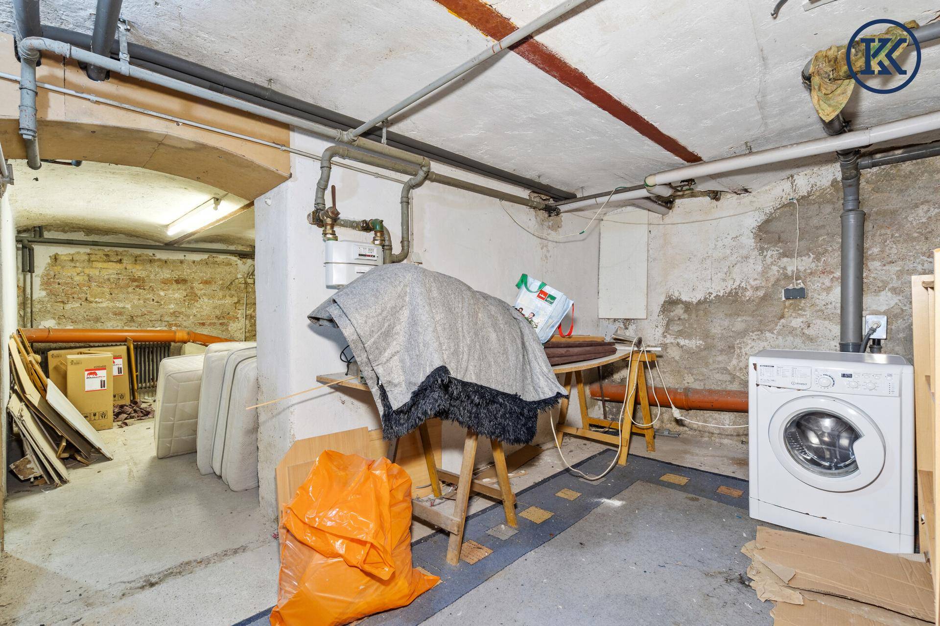 Kellerraum mit Waschmaschine, sichtbaren Rohren und Lagerflächen für diverse Gegenstände.