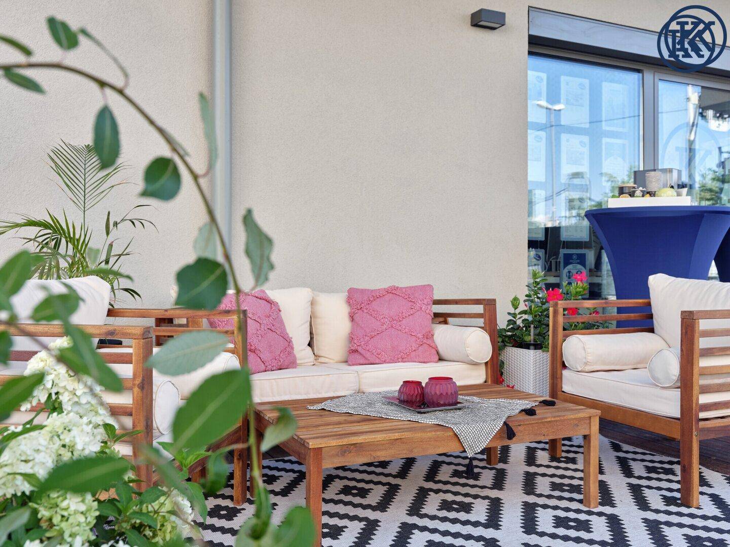 Nahaufnahme einer Terrasse mit bequemen Holzmöbeln, rosa Kissen und einem gemusterten Teppich.