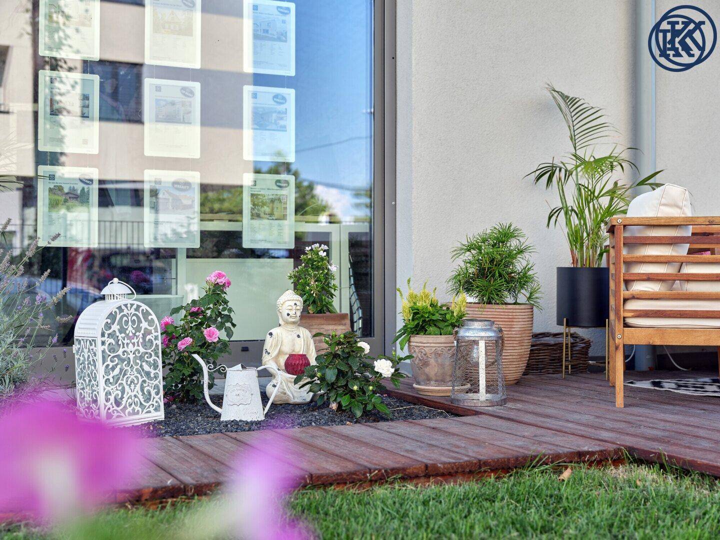 Detailansicht einer Terrasse mit Holzdielen, dekorativen Elementen und Pflanzen vor einer Glasfront.