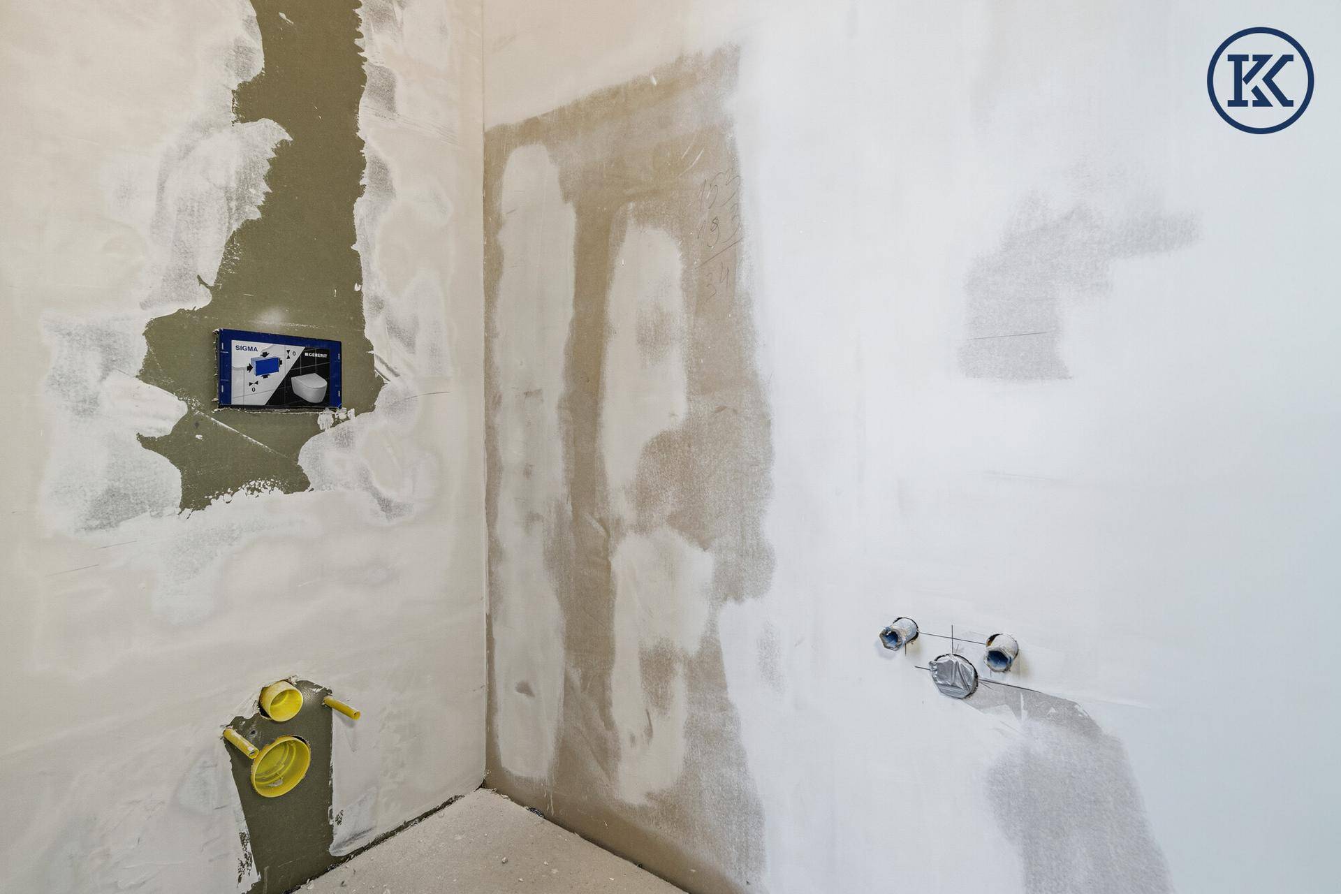 Badezimmer im Rohbau mit vorbereiteten Anschlüssen für Toilette und Waschbecken.