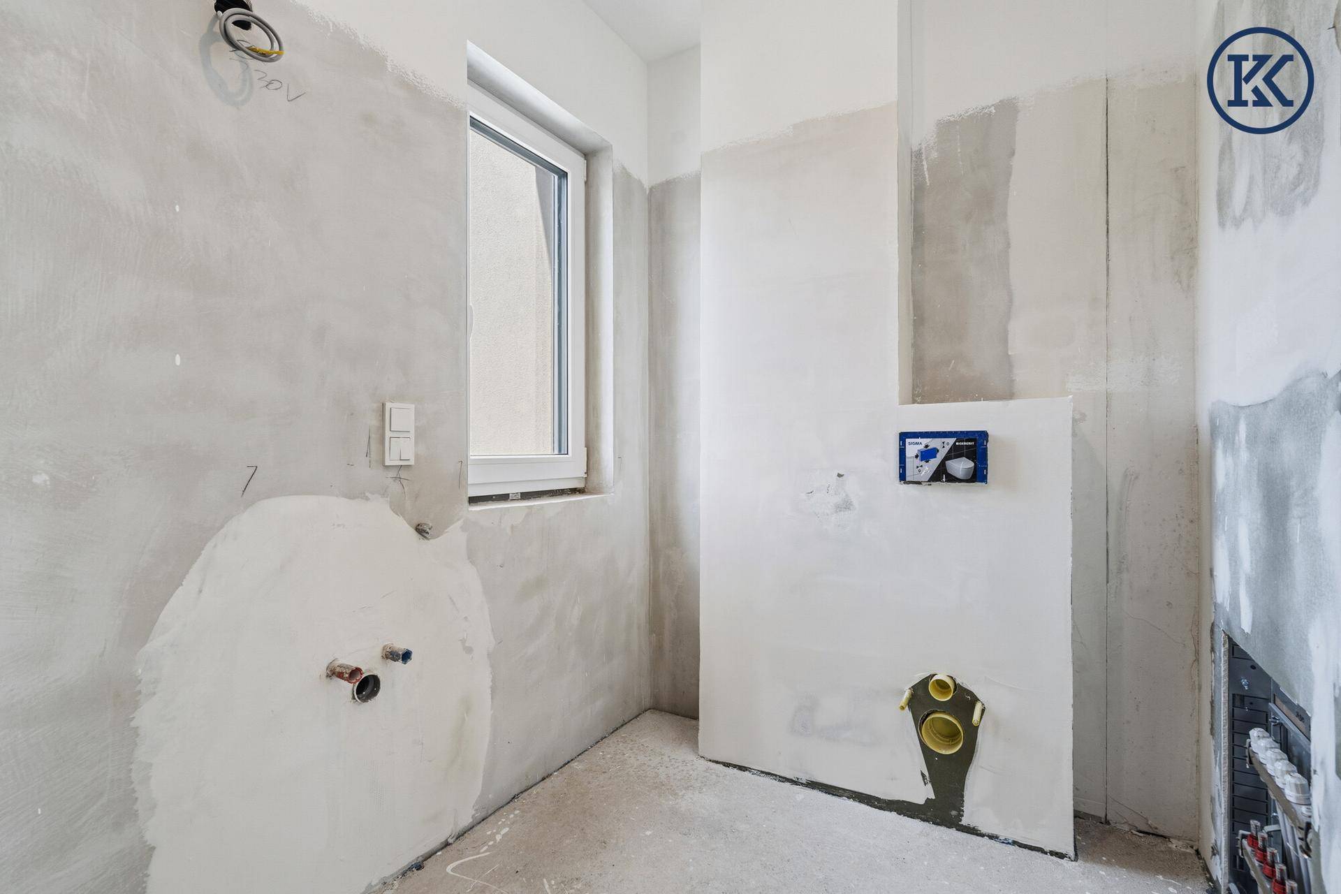 Badezimmer im Rohbau mit Fenster und vorbereiteten Anschlüssen für die Sanitäreinrichtung.
