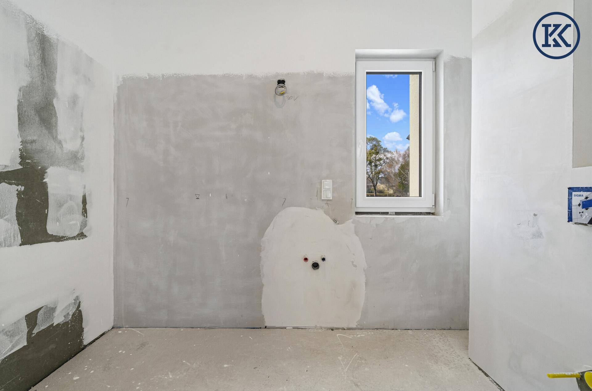Badezimmer im Rohbau mit Fenster und vorbereiteten Anschlüssen für Dusche und Waschtisch.