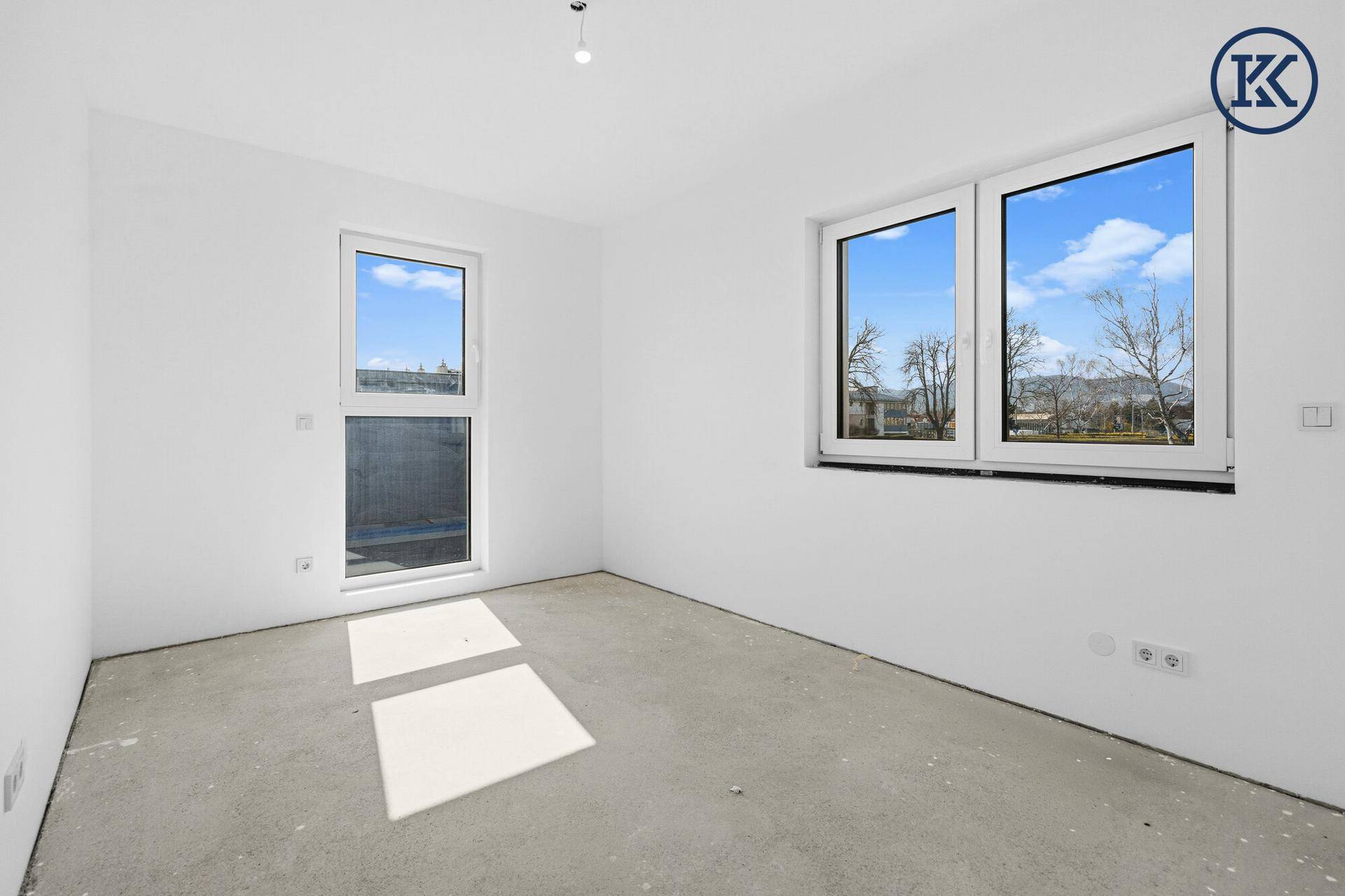 Unmöblierter Raum im Rohbau mit großen Fenstern und Zugang zu einem möglichen Balkon.