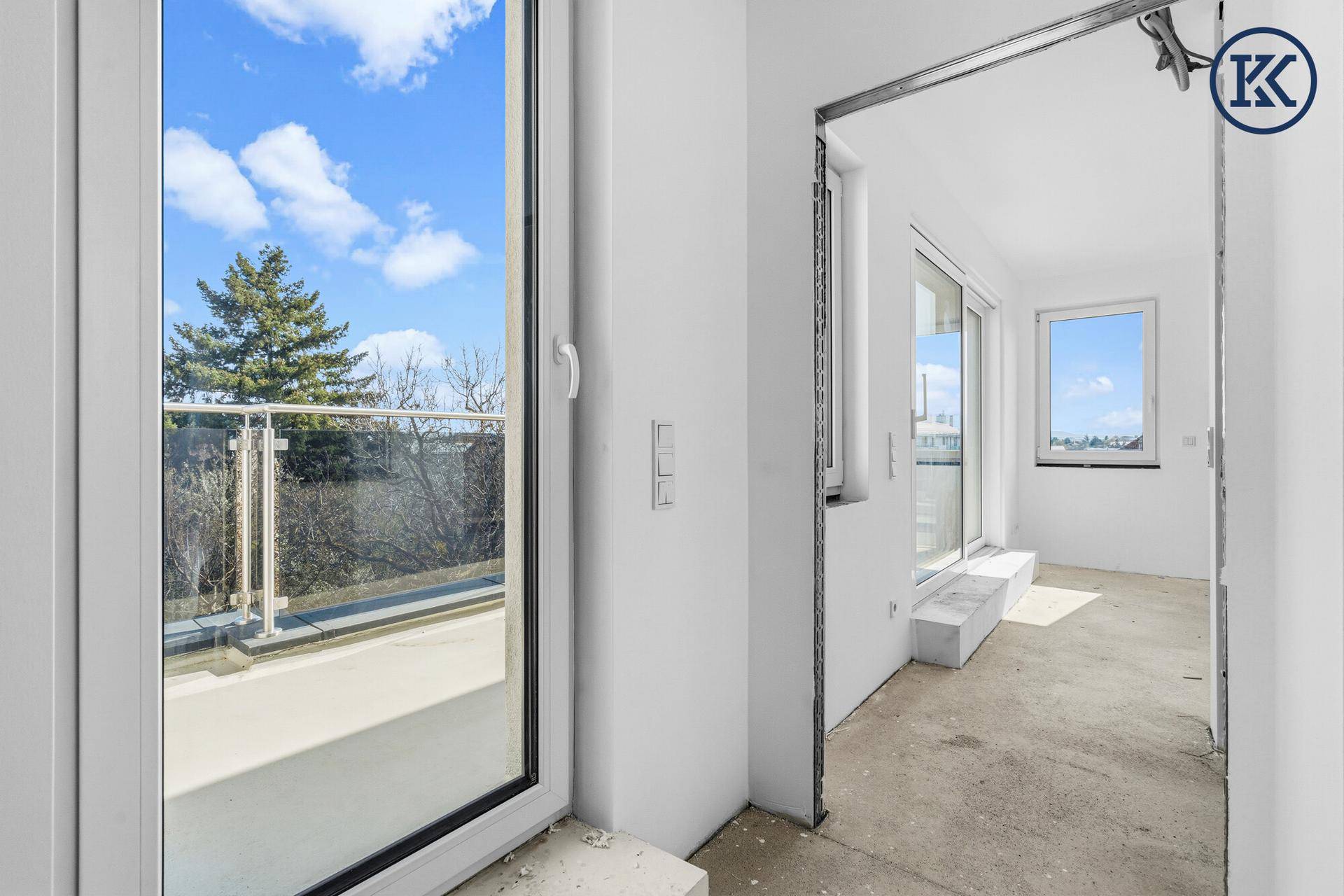 Heller Raum im Rohbau mit großem Fenster und Zugang zu einem Balkon.