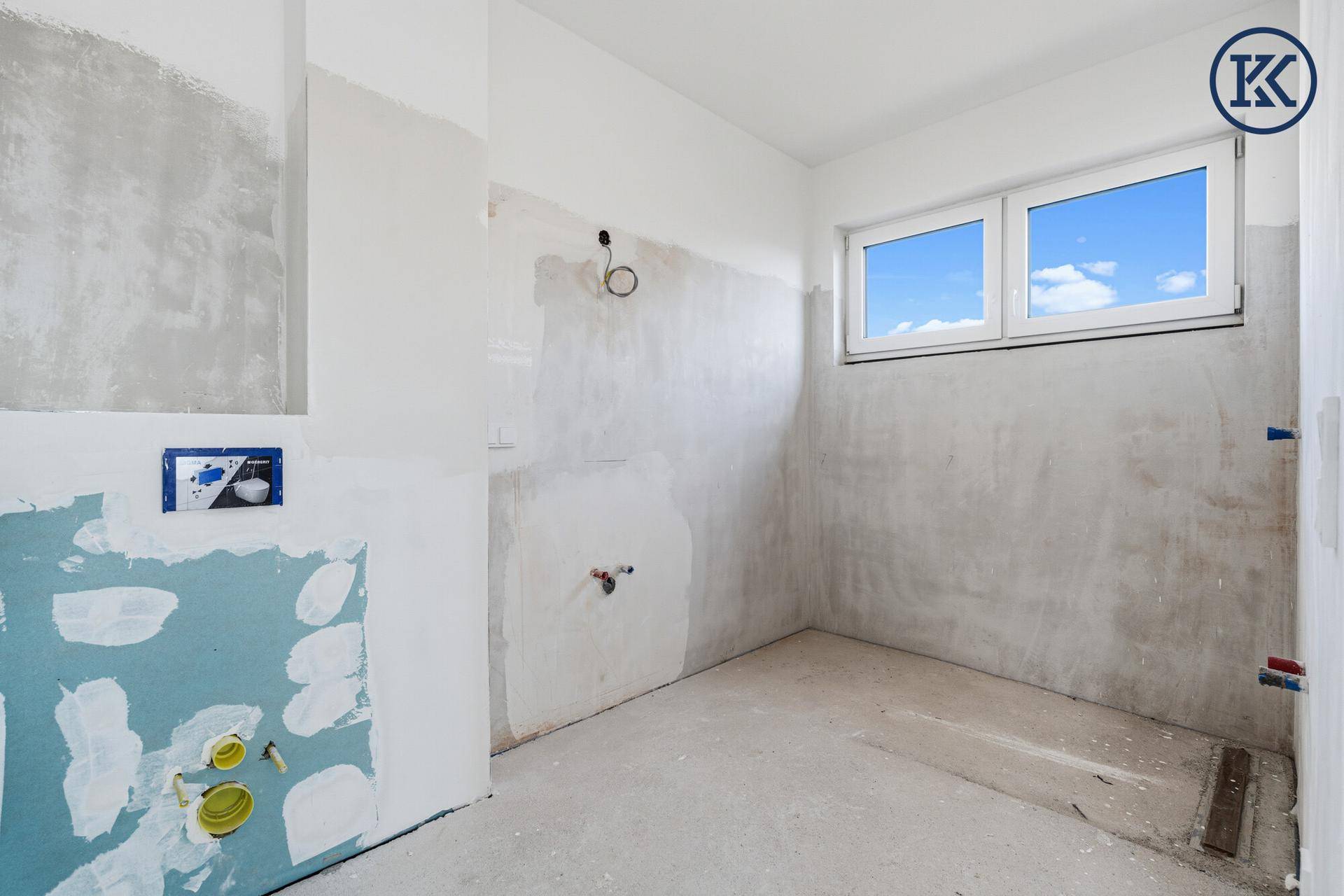 Badezimmer im Rohbau mit Fenster und vorbereiteten Anschlüssen für die Sanitäreinrichtung.