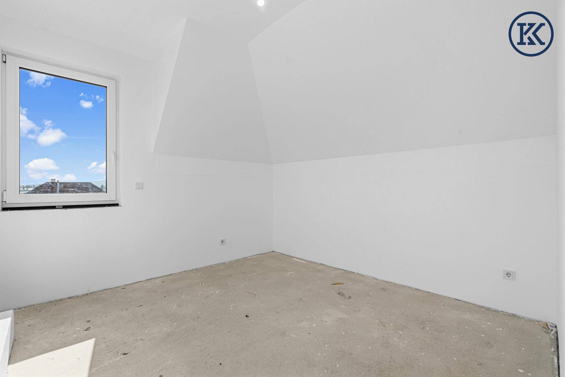 Unmöblierter Raum im Dachgeschoss im Rohbau mit Fenster und Dachschräge.