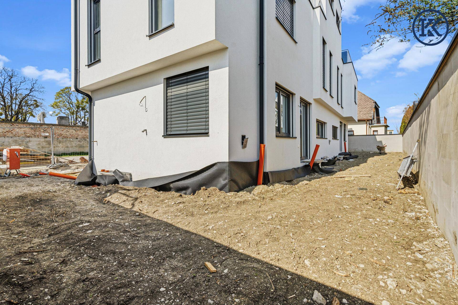 Seitenansicht des Hauses mit Gartenbereich im Rohbau und vorbereiteten Drainagearbeiten.