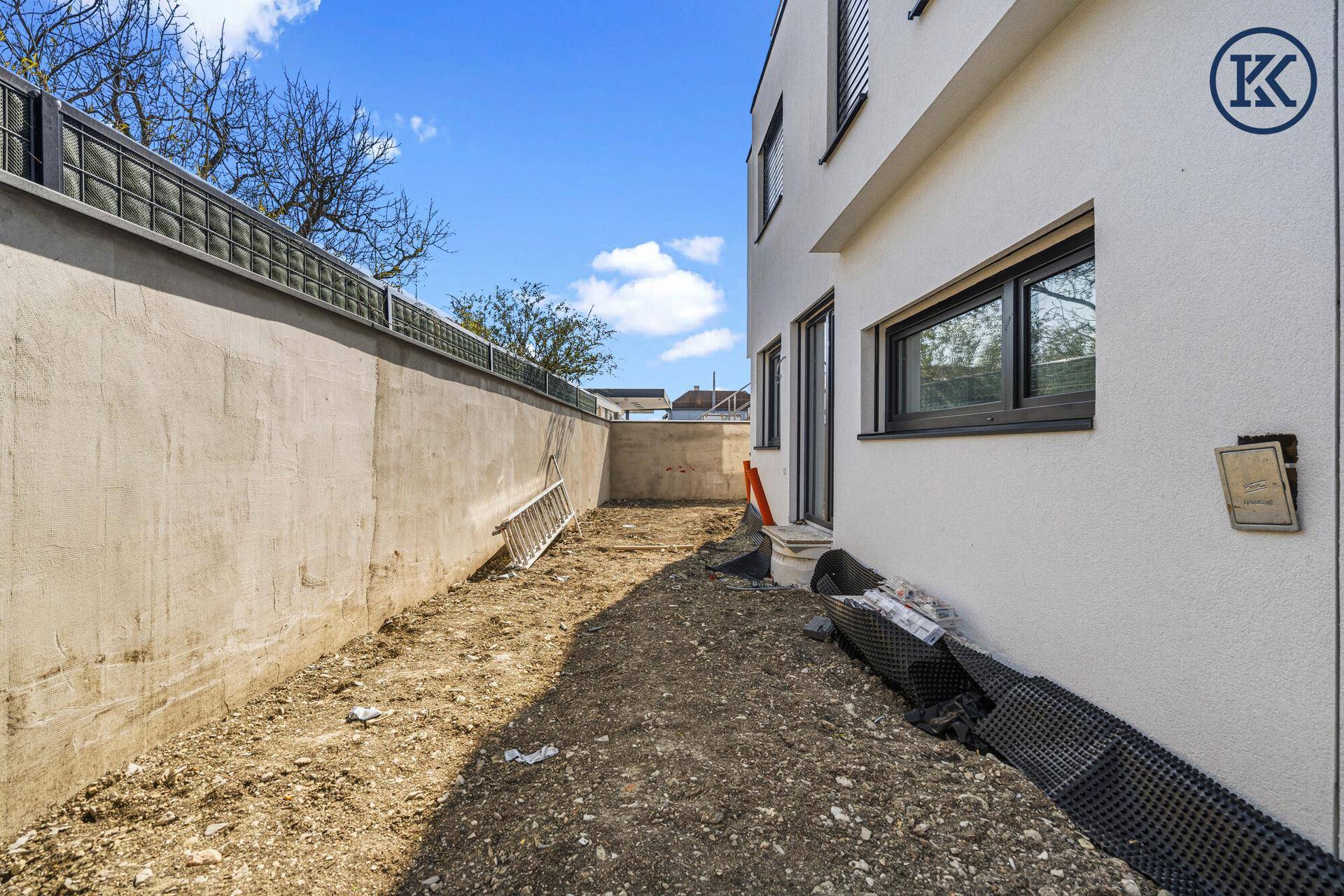 Gartenbereich im Rohbau mit hoher Mauer und unfertigem Gelände, bereit zur Gestaltung.