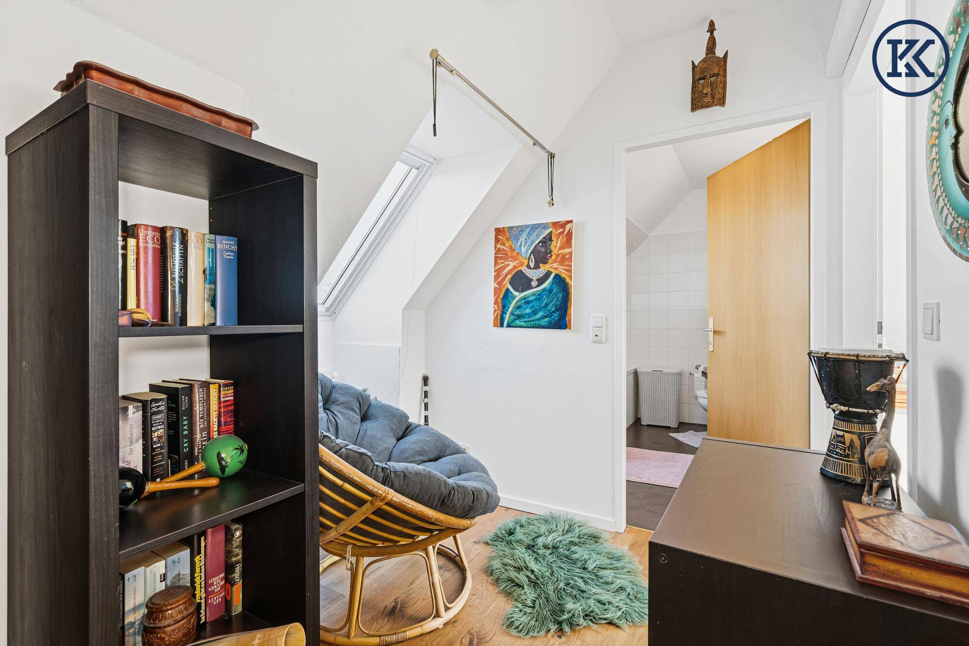 Kleiner Arbeitsbereich im Dachgeschoss mit Holzboden, Bücherregal und Dachfenster.