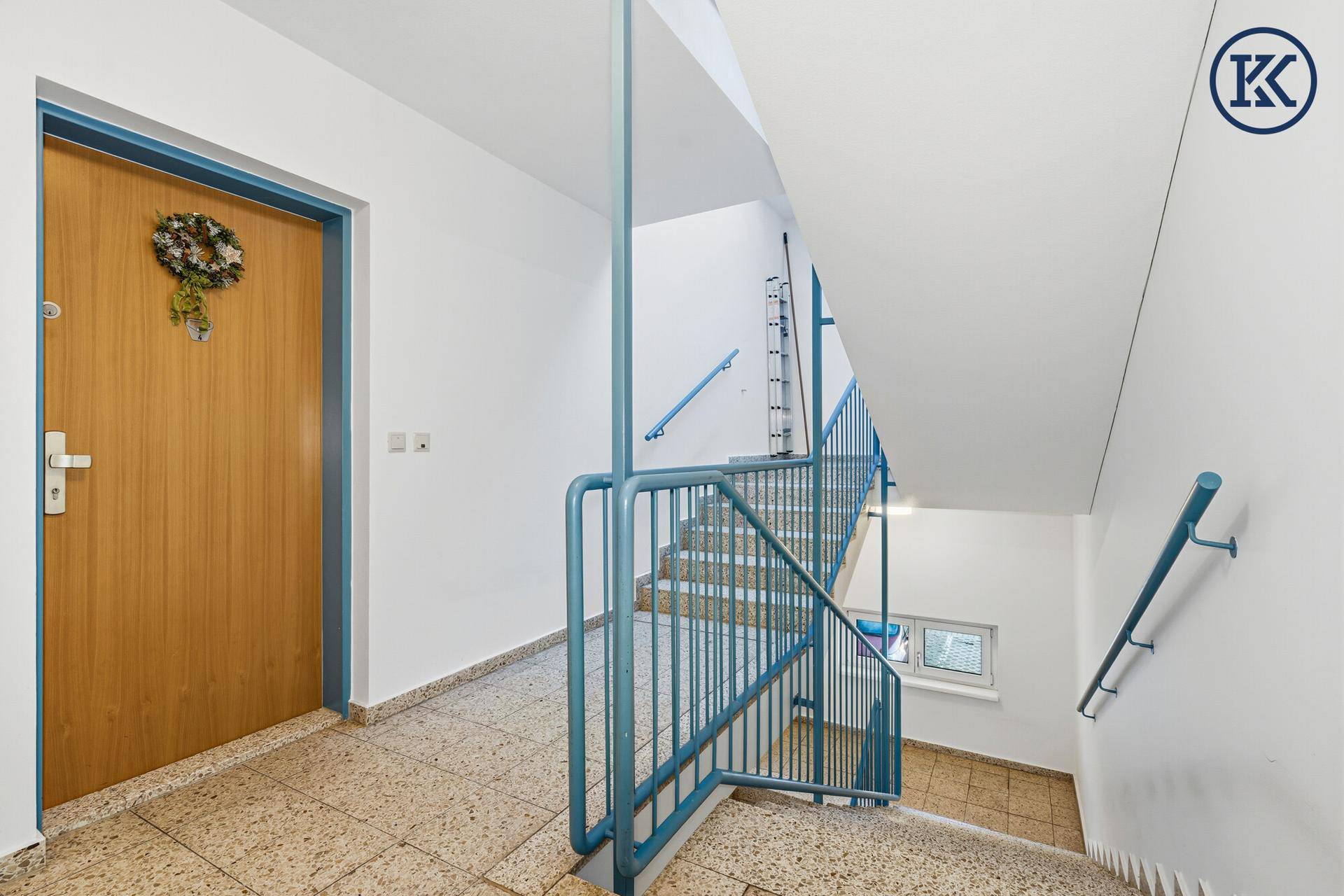 Gemeinschaftliches Treppenhaus mit Terrazzoboden und blauen Geländern.