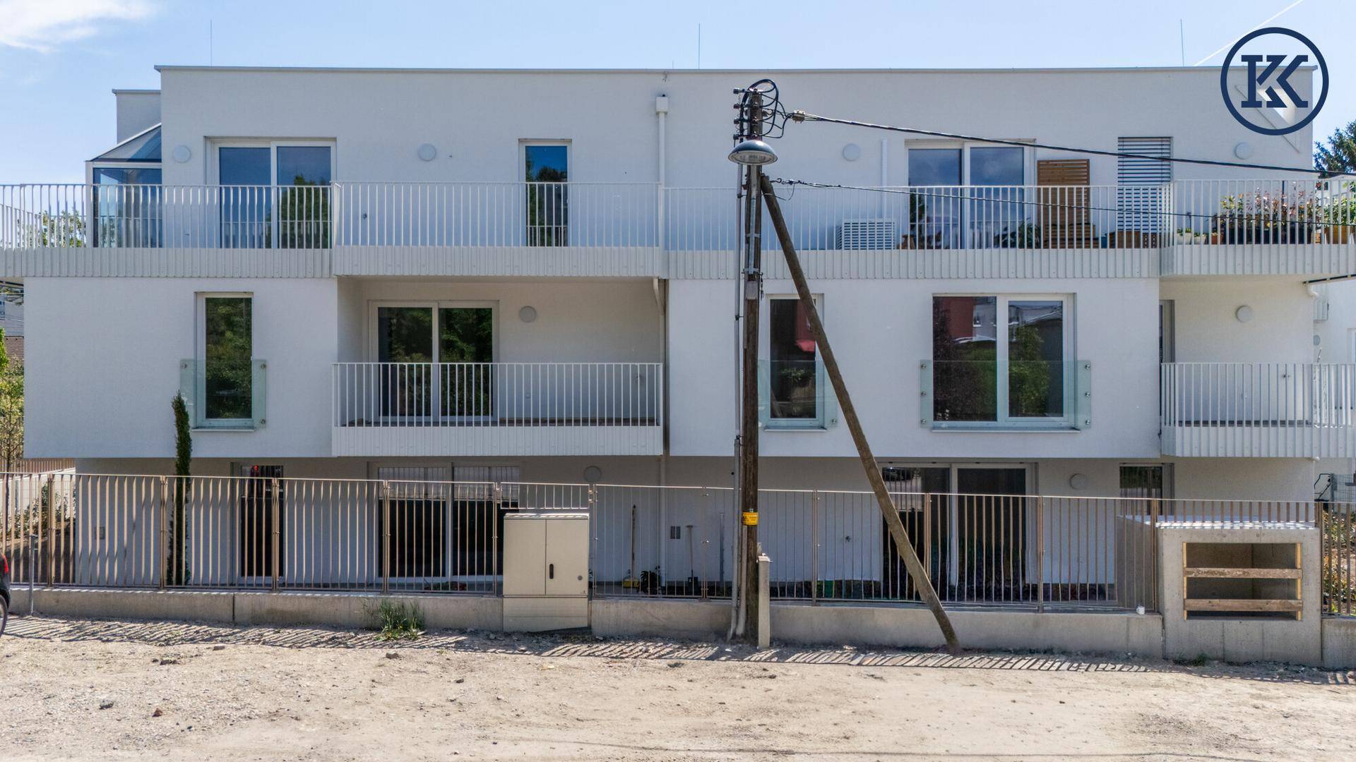 Frontansicht der modernen Wohnanlage mit weißen Balkonen und großen Fenstern von der Straße aus.