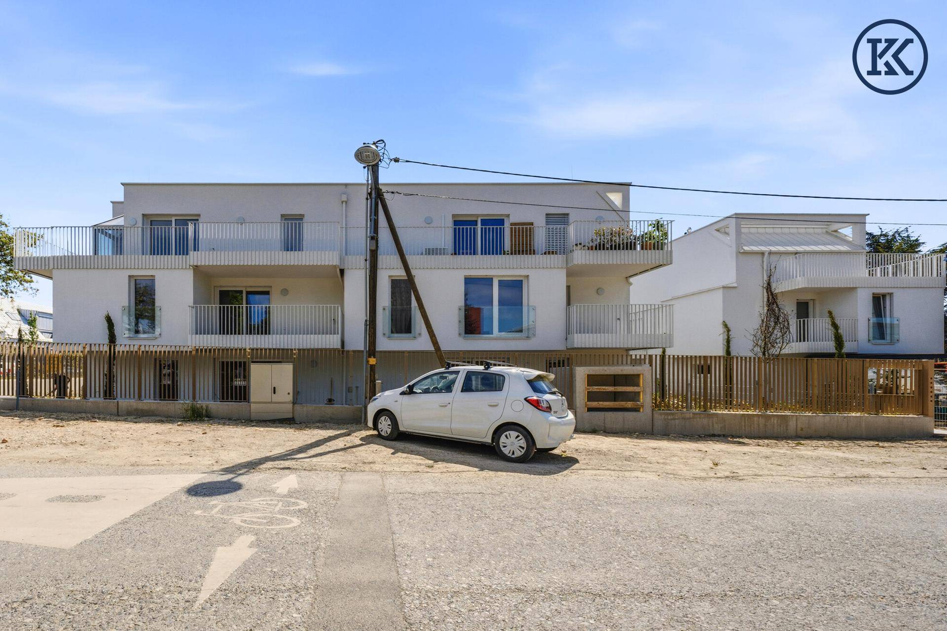 Ansicht der modernen Wohnanlage von der Straße mit Balkonen und einer weißen Fassade unter blauem Himmel.