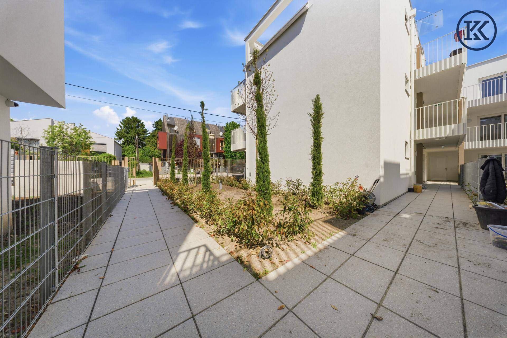 Gepflasterter Weg zwischen den modernen Gebäuden mit jungen Pflanzen und Metallzäunen.