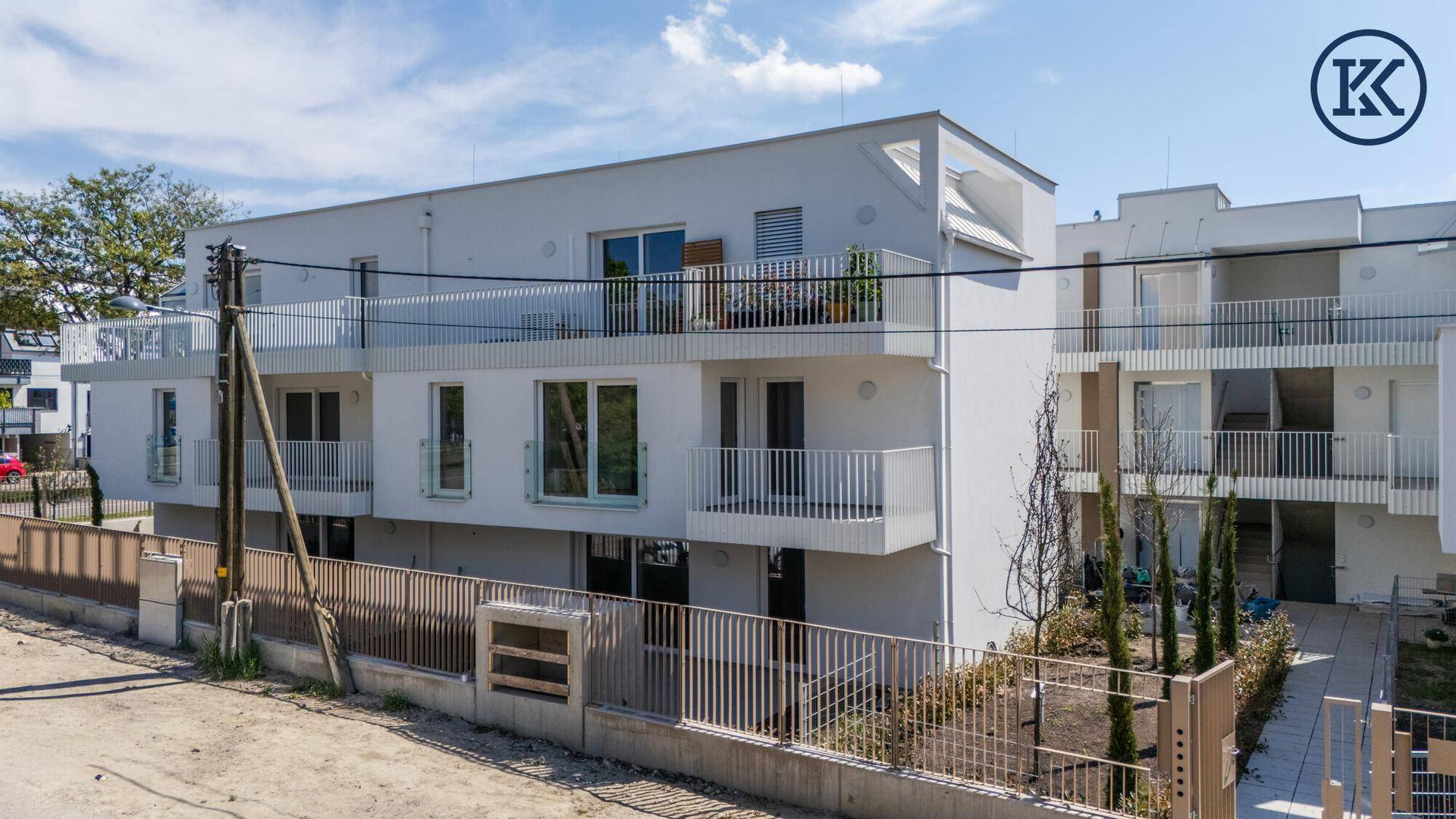 Moderne Wohnanlage von der Straße aus gesehen mit Balkonen und einer weißen Fassade.