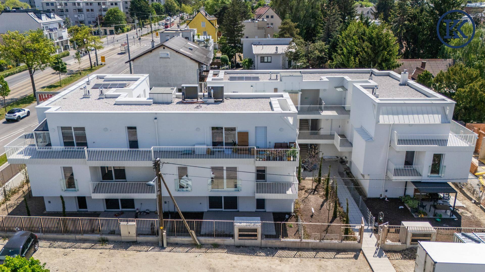 Luftaufnahme eines modernen Wohnkomplexes mit Flachdächern, Balkonen und umliegender Infrastruktur.