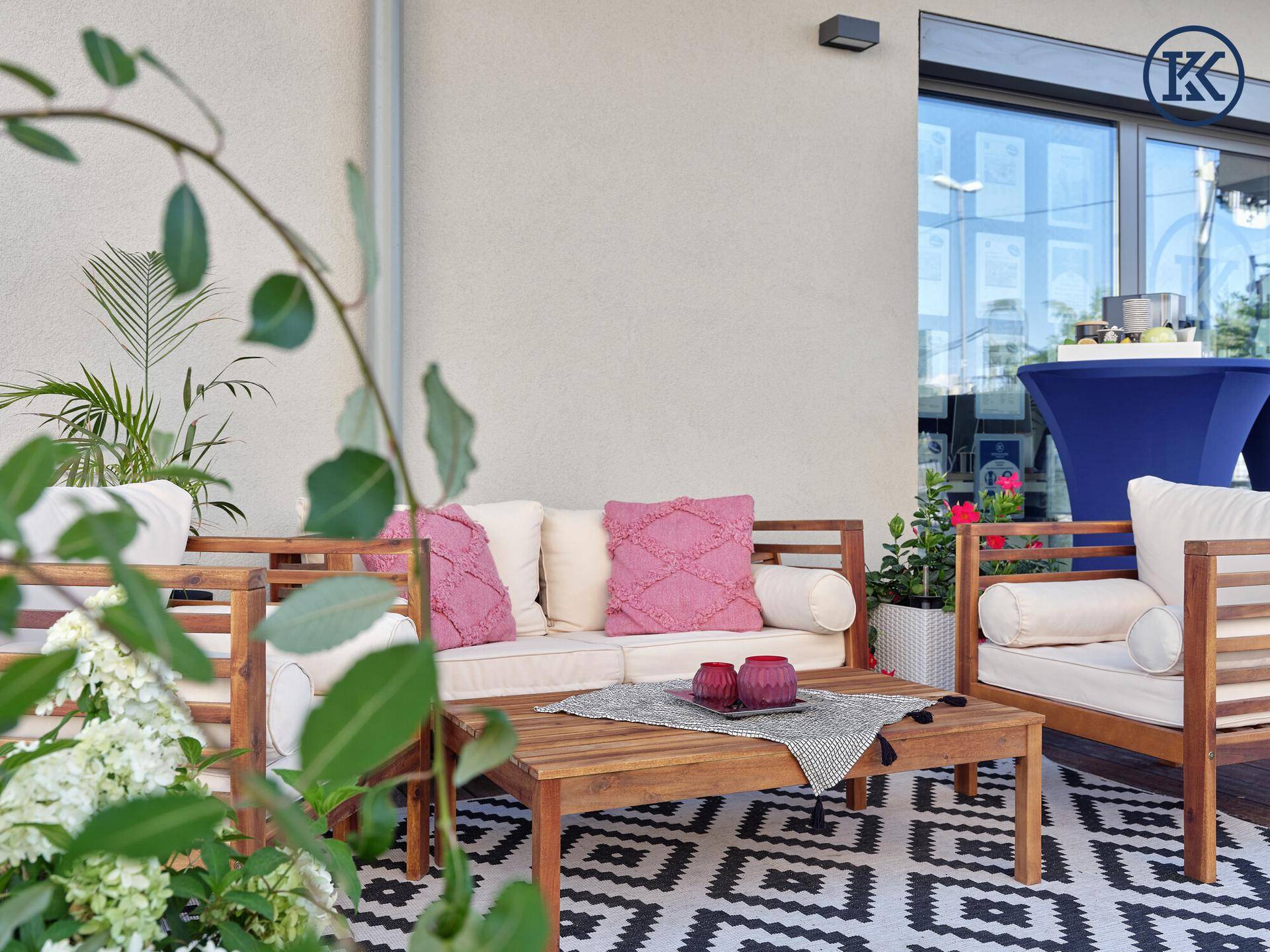 Nahaufnahme der Terrasse mit bequemen Holzmöbeln, rosa Kissen und einem modernen Teppich vor der Glasfassade.