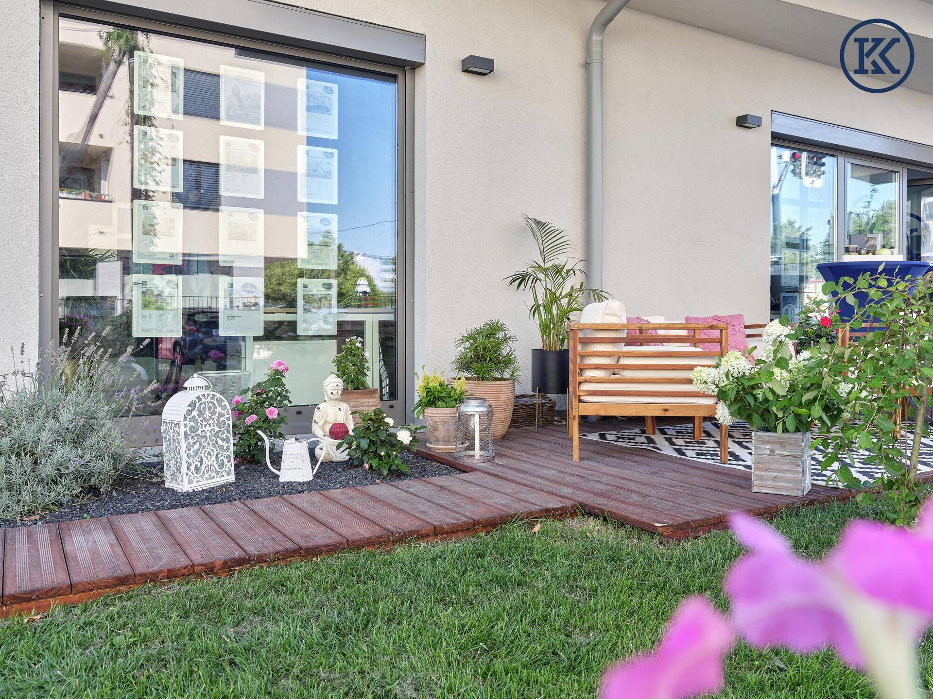 Weitwinkelansicht der Terrasse mit Rasenfläche, modernen Fenstern und Außenrollläden am Gebäude.