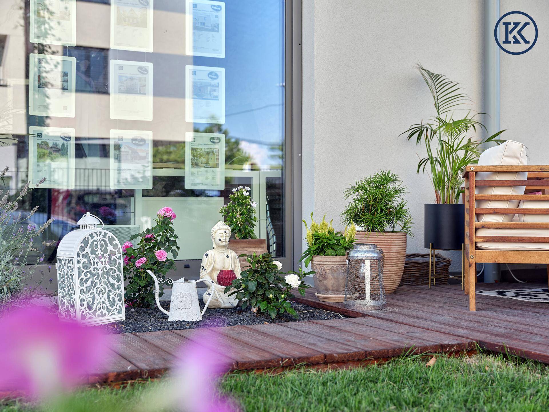 Detailansicht der Terrasse mit dekorativen Laternen, Pflanzen und einer großen Glasfassade des Gebäudes.