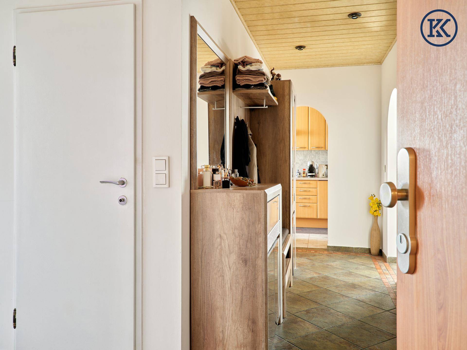 Eingangsbereich mit Holzdecke, Garderobe und Blick auf die Küche durch einen Bogen.