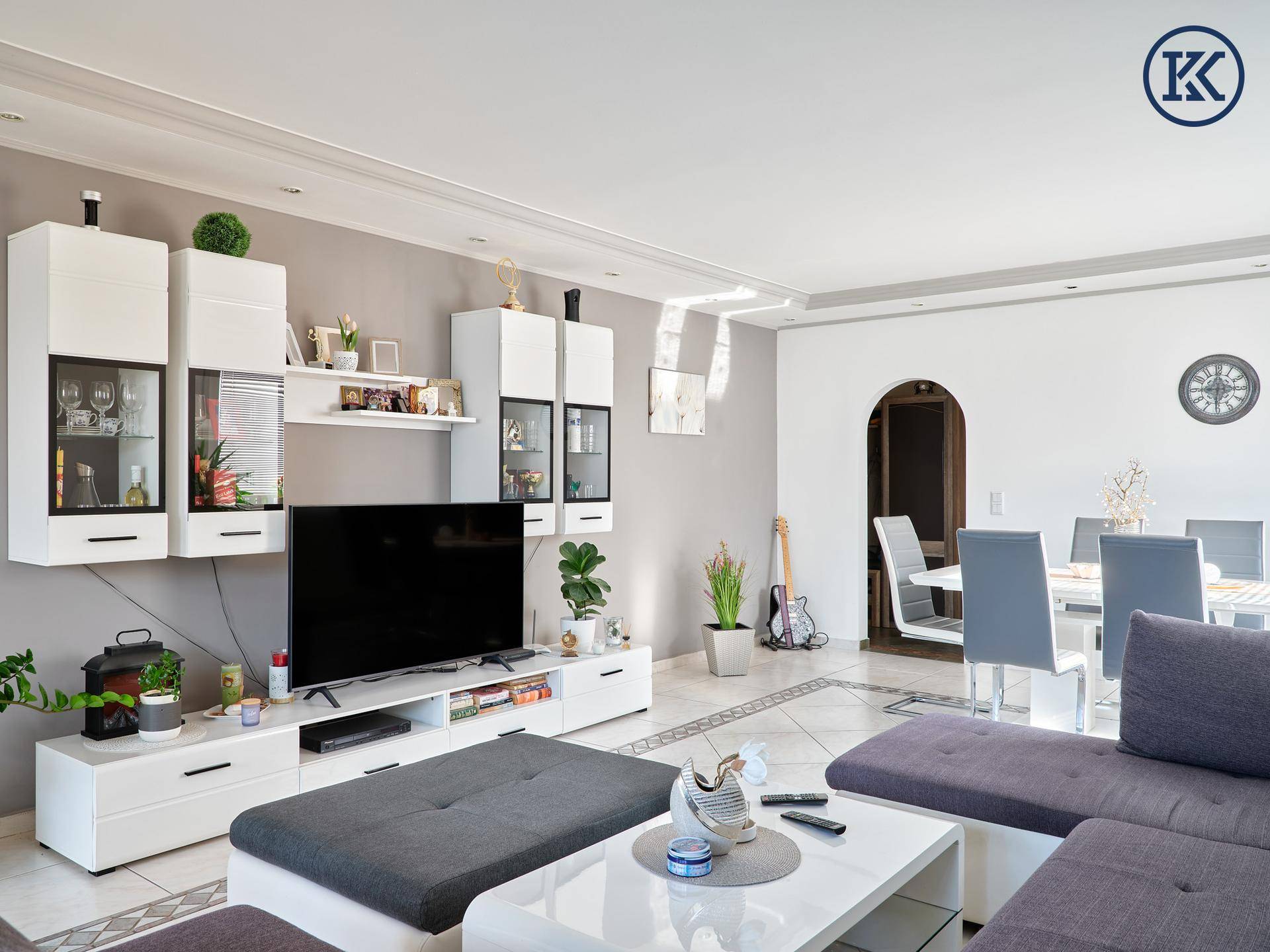 Moderner Wohnbereich mit TV-Möbeln, Sofa und Essbereich im Hintergrund durch einen Bogen.