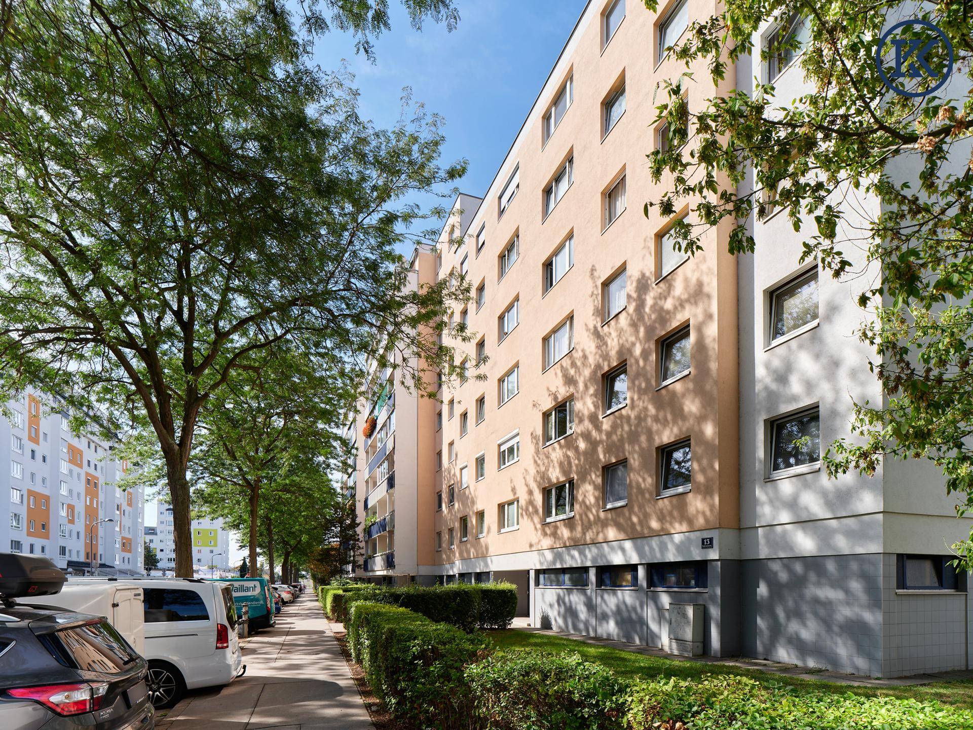 Mehrfamilienhaus mit moderner Fassade, umgeben von Bäumen und Grünflächen an einer Straße.