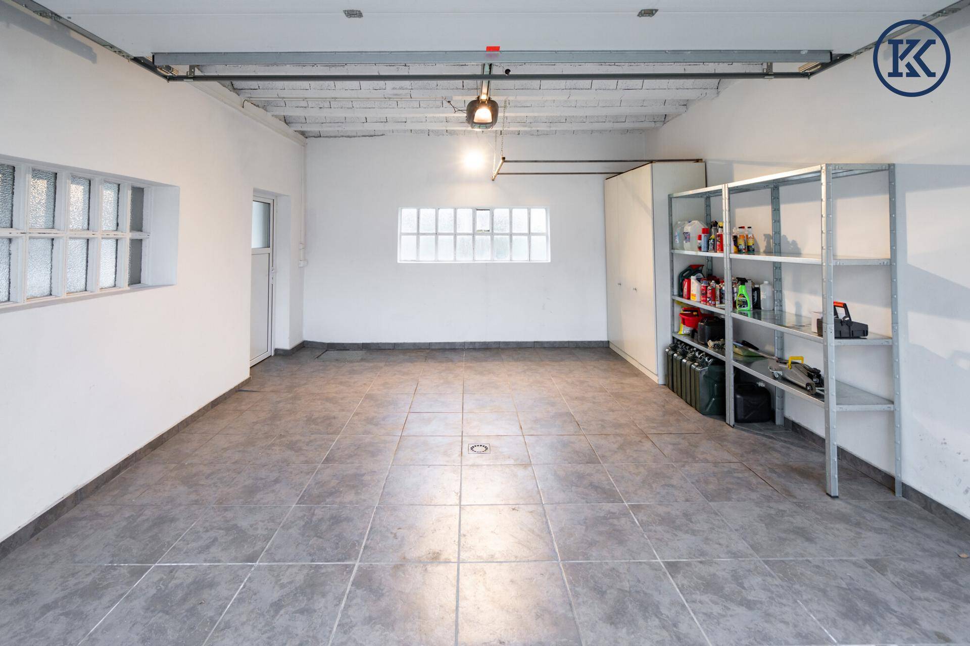 Helle Garage mit Fliesenboden, weißen Wänden und praktischen Lagerregalen.