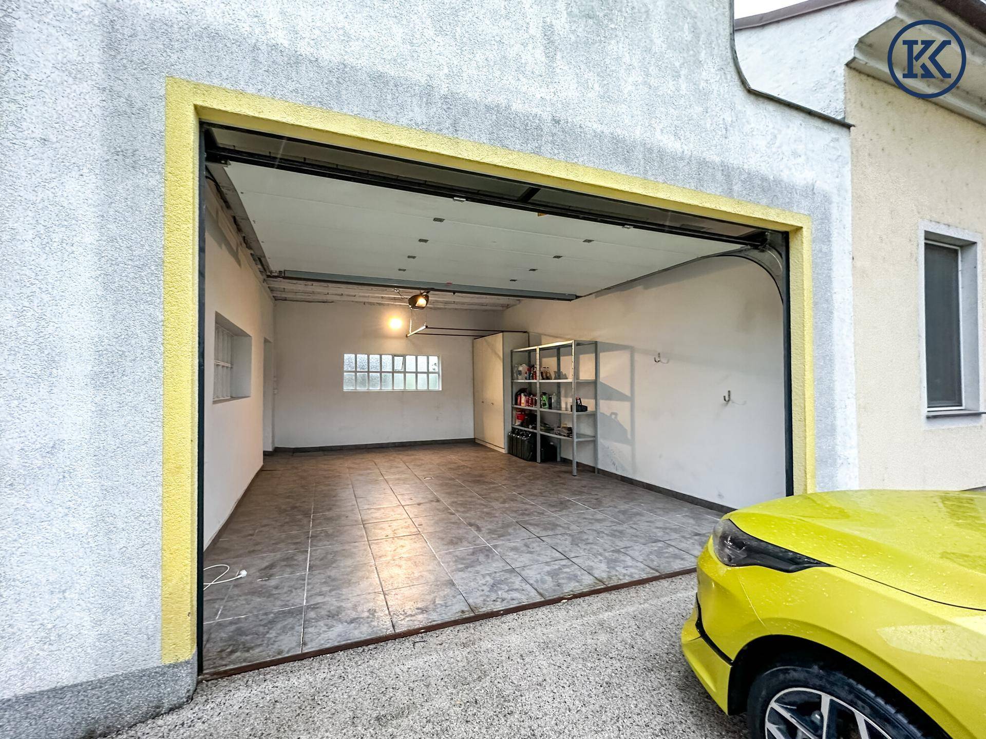 Geräumige Garage mit Fliesenboden, Regalen und offenem Tor.