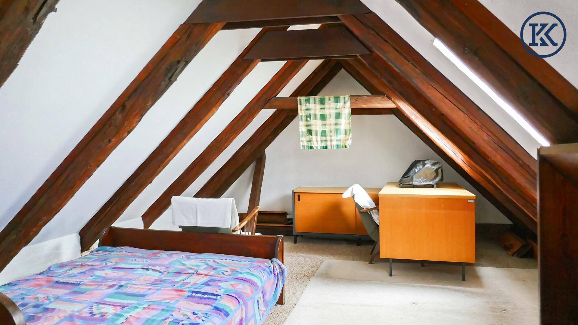 Schlafzimmer im Dachgeschoss mit sichtbaren Holzbalken, Bett und Schreibtisch.