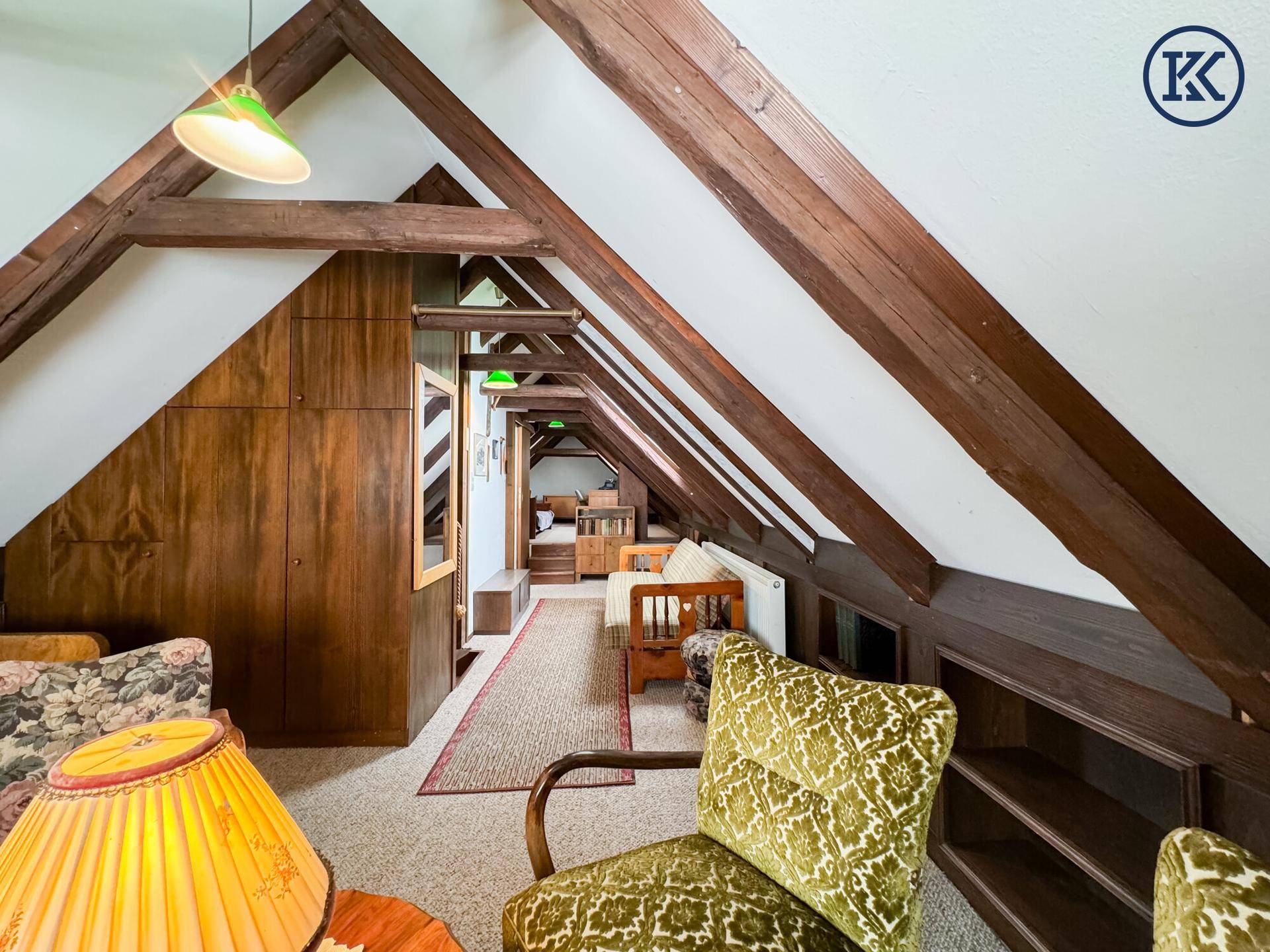 Gemütlicher Dachbodenbereich mit sichtbaren Holzbalken, Teppichboden und integrierten Holzschränken.